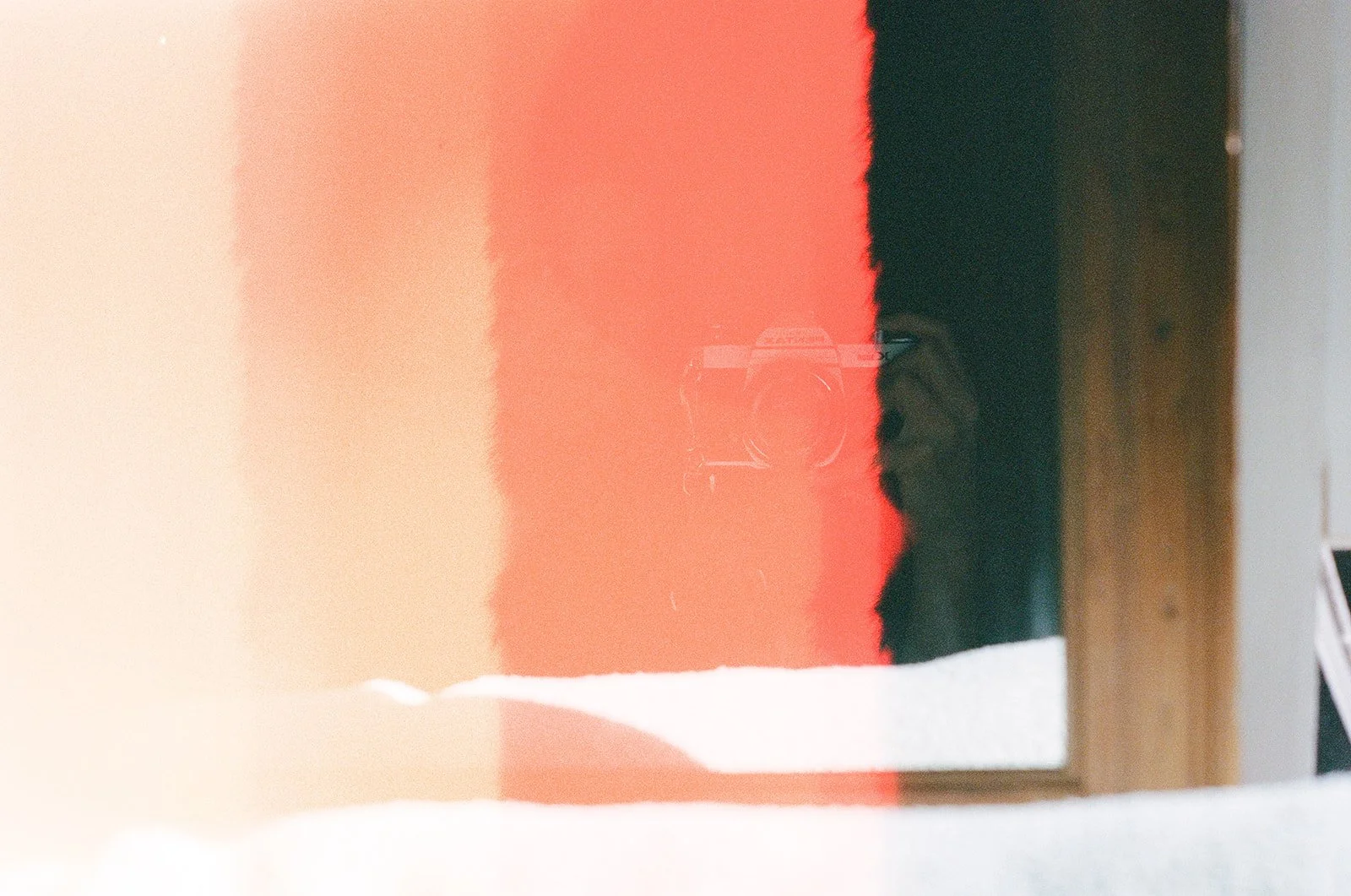 A reflection of a person taking a photo with a camera in a mirror, with a vertical strip of red light and some background objects visible.