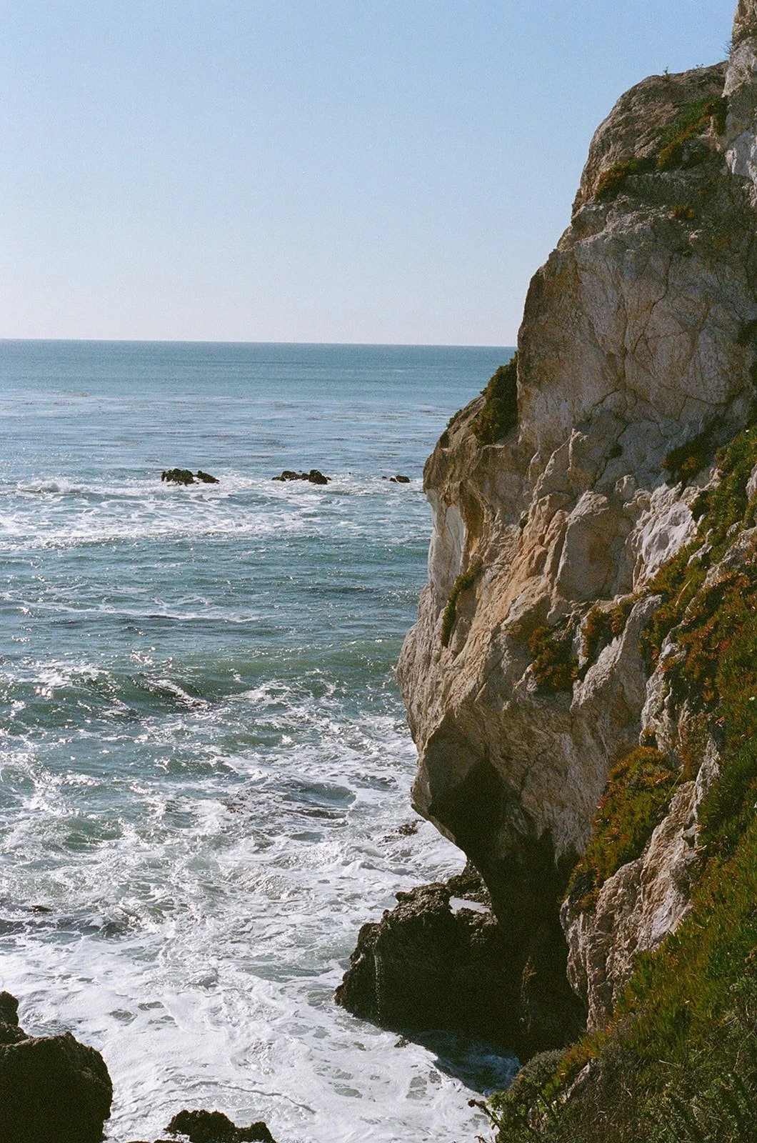Ocean waves crashing against rocky cliffs on a clear day.
