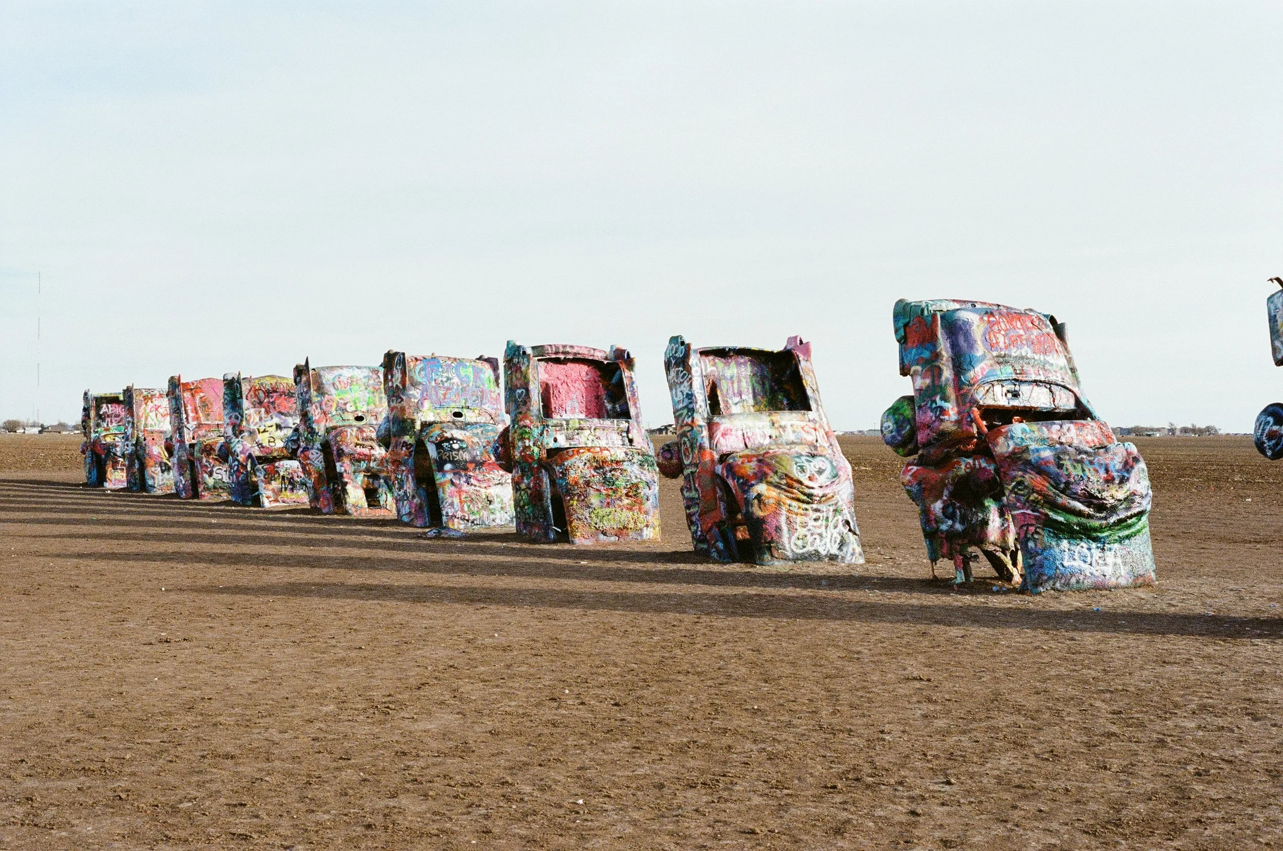 Line of sculptures resembling trucks covered in colorful graffiti in a desert landscape.