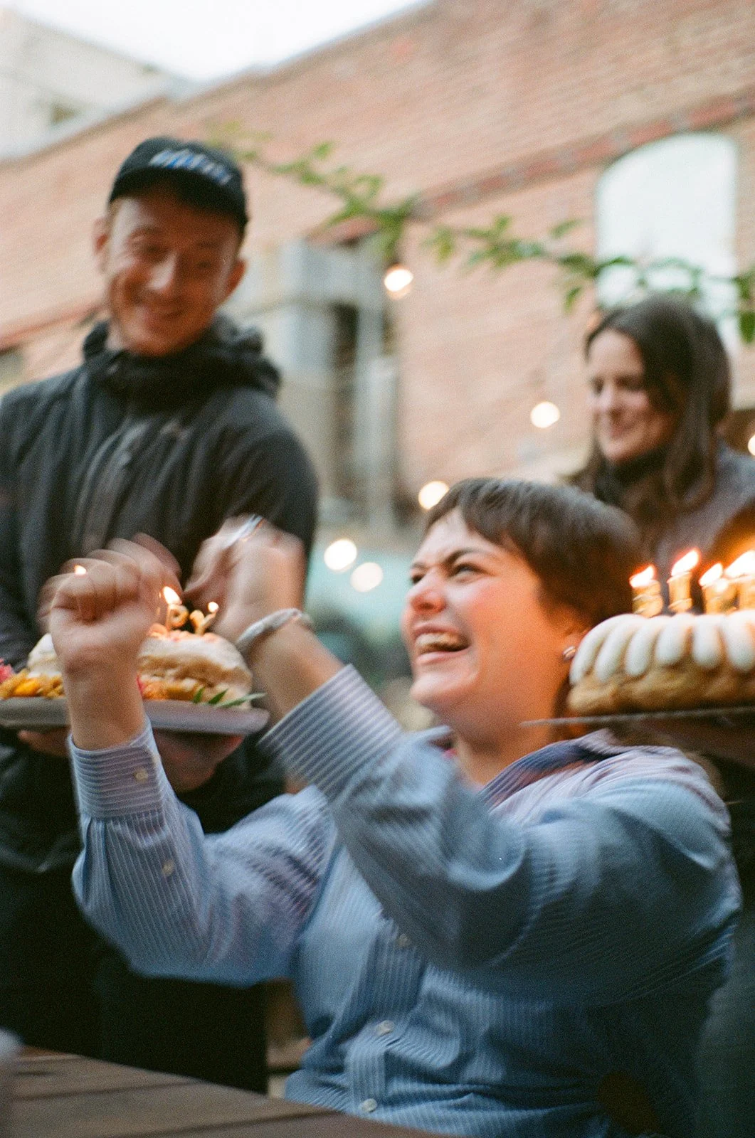 A woman celebrates her birthday with friends, holding a cake with lit candles, while others cheer and smile at the celebration.