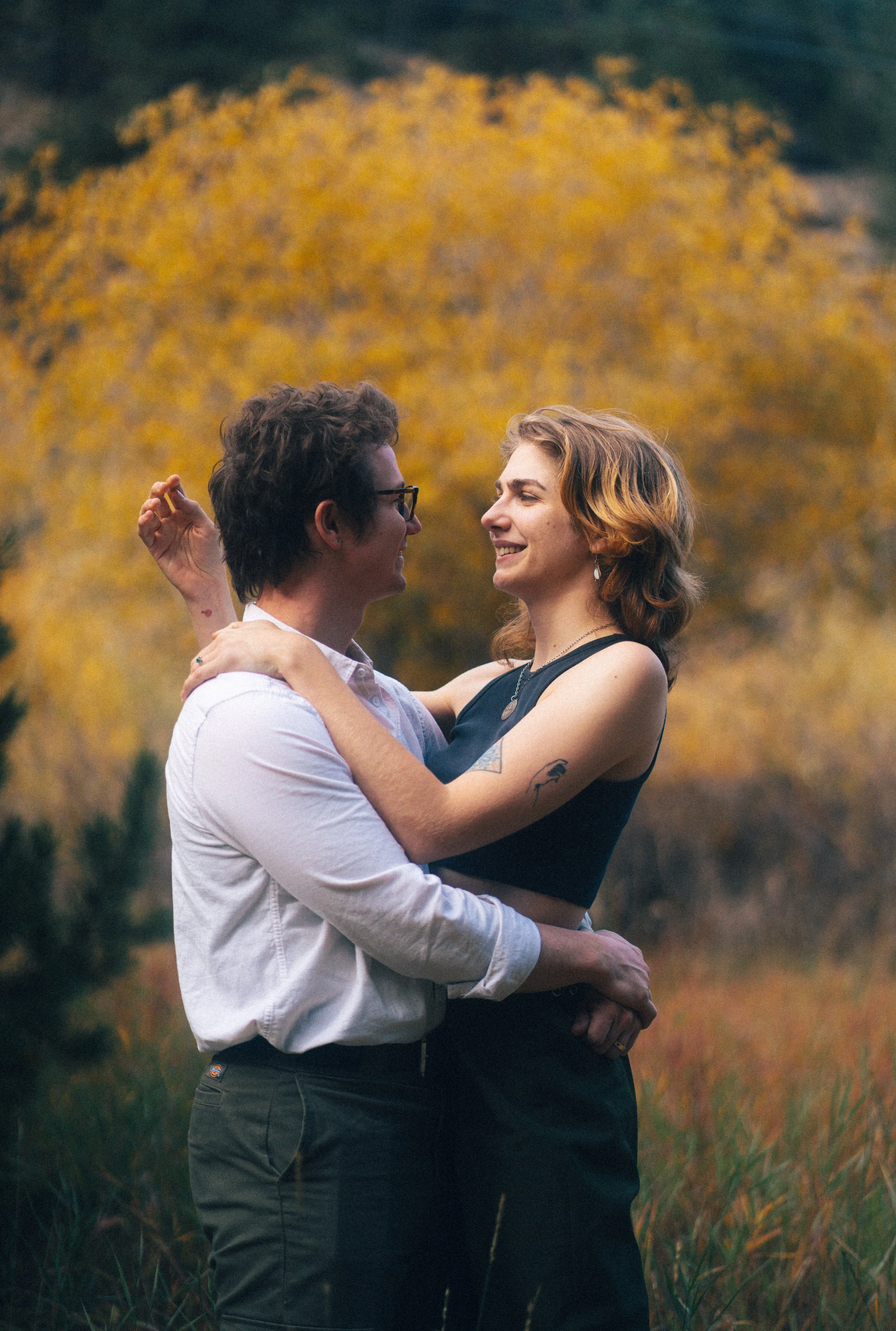 A couple dancing outdoors in a field of tall grass with autumn trees in the background.