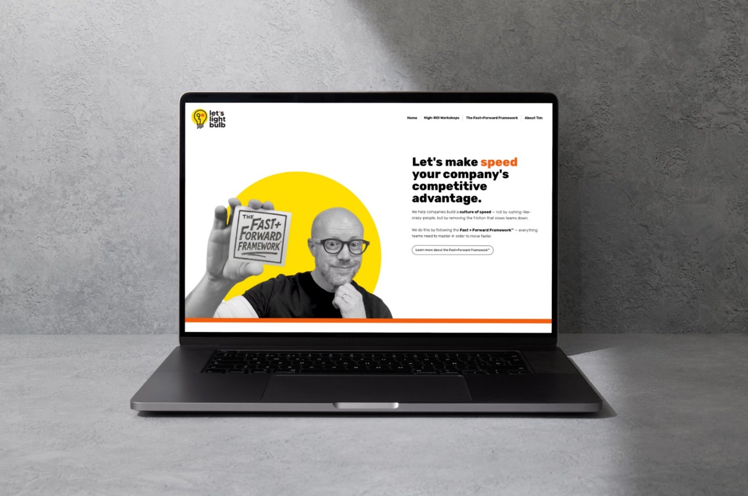 Laptop on a concrete surface displaying a website about a framework for improving company speed, featuring a man holding a sign with the framework's name on it.