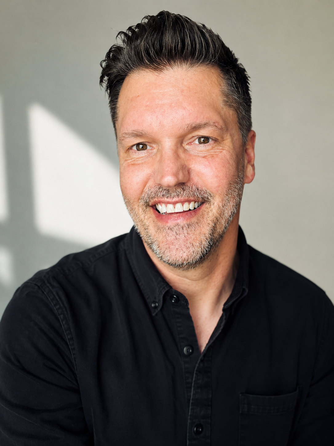 Headshot of Brad Gantt, smiling, wearing a black button-up shirt, against a neutral background.