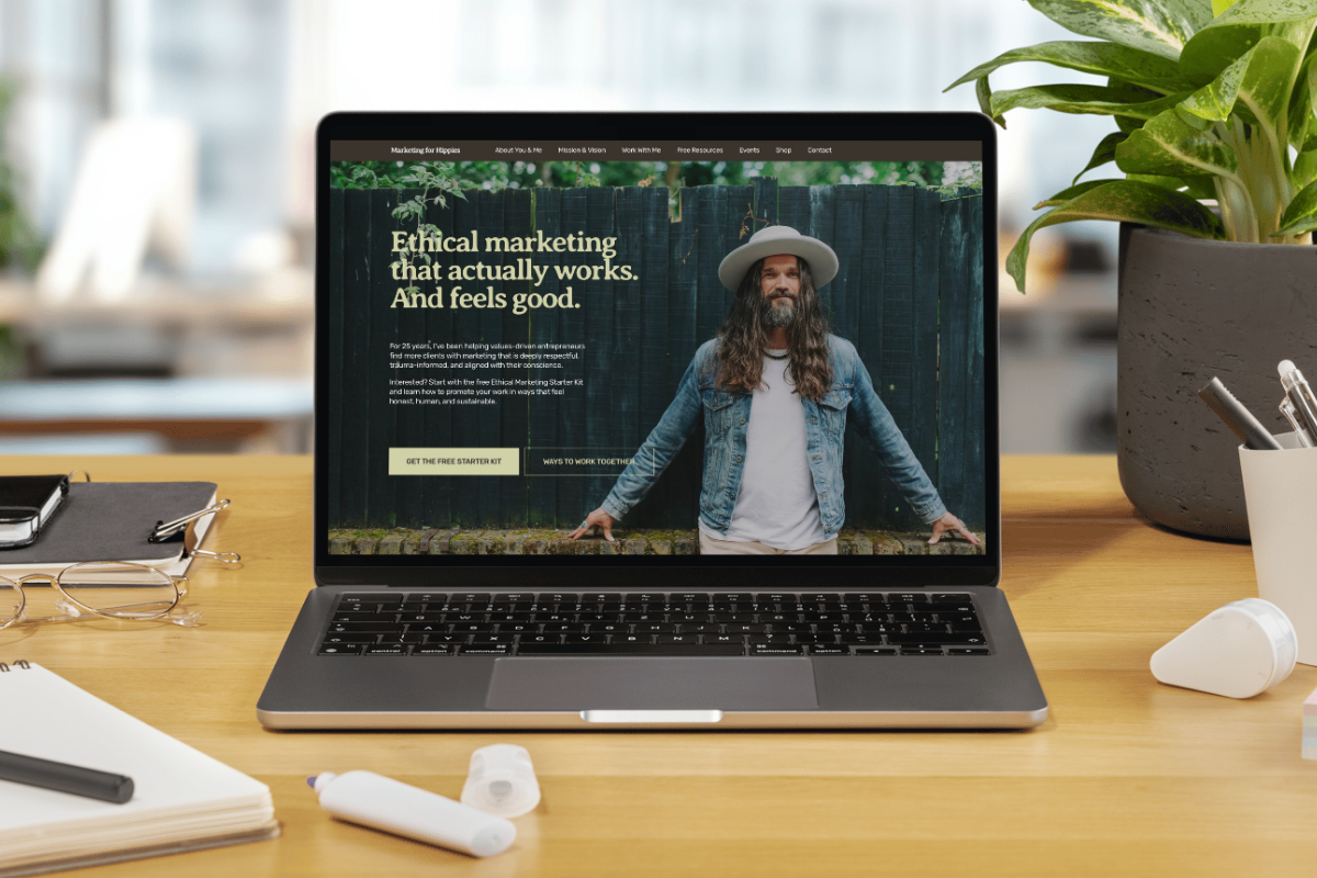 Laptop on a wooden desk displaying a website about ethical marketing with a man in a denim jacket and hat in front of a wooden fence.