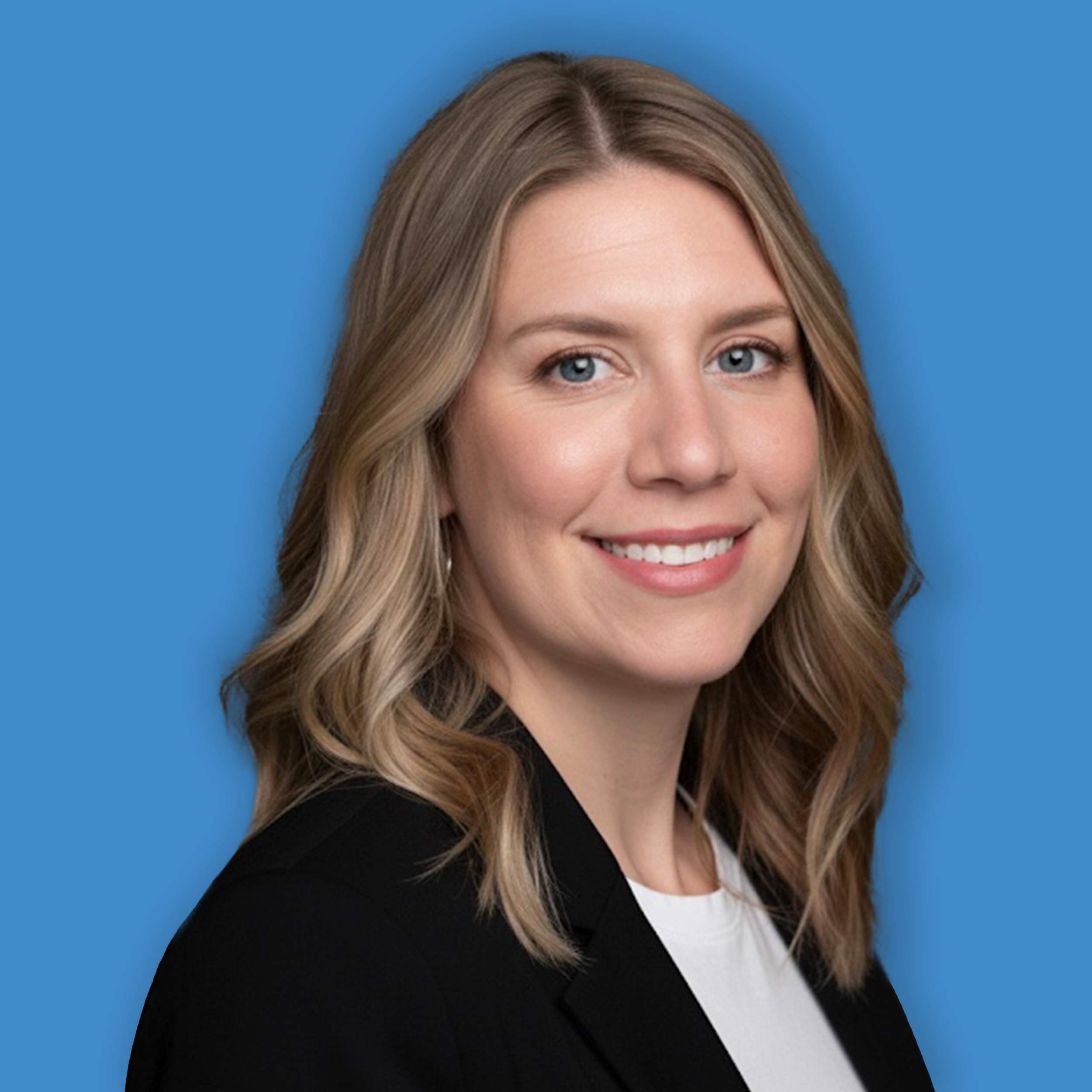 Close-up of a woman with blonde wavy hair, blue eyes, smiling, wearing a black blazer and a white shirt, against a blue background.