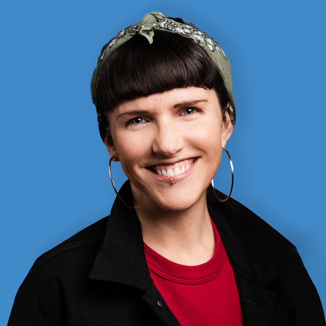 Portrait of a smiling woman with short dark hair, wearing a green bandana, hoop earrings, a red shirt, and a black jacket against a blue background.