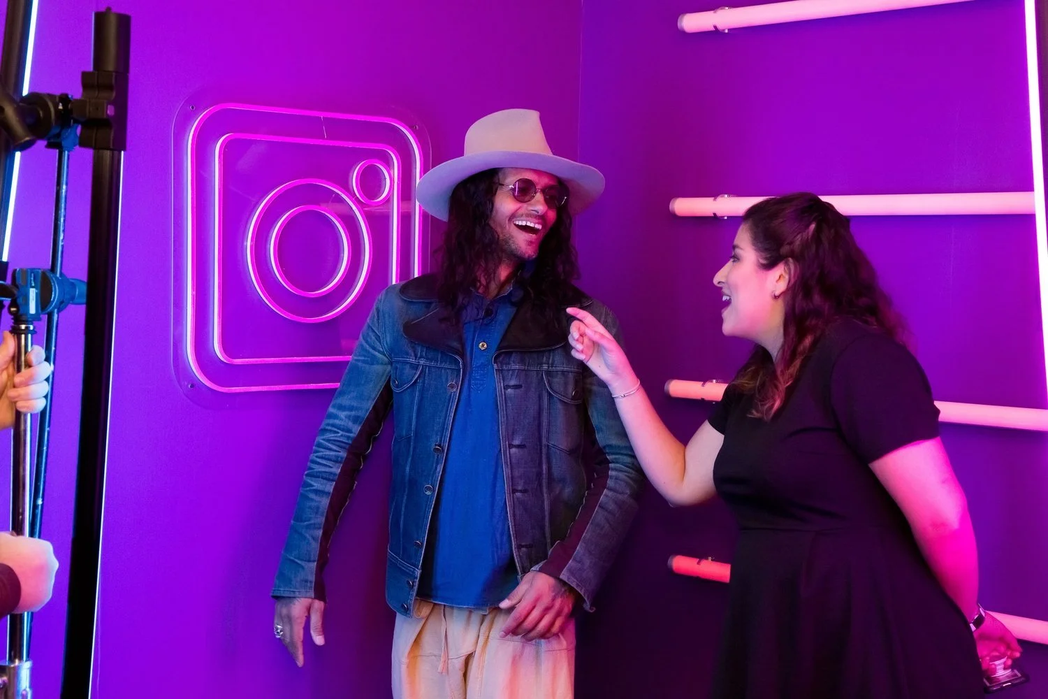 Two people smiling and talking in front of neon pink Instagram logo with purple lighting background.