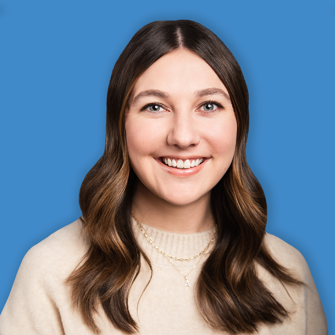 Portrait of a young woman with long, wavy brown hair smiling against a blue background.