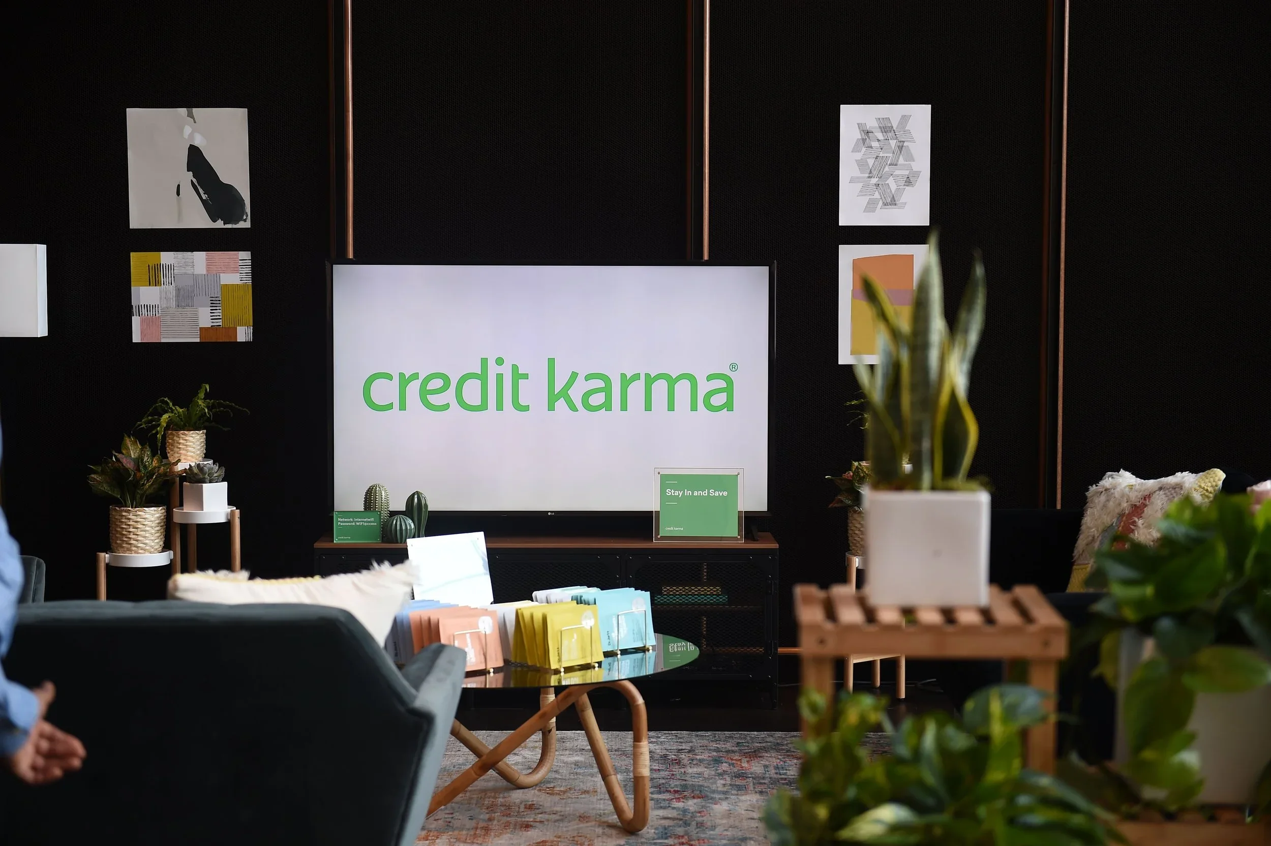 An interior scene with a display that reads 'credit karma,' surrounded by plants, artwork on the walls, and furniture.