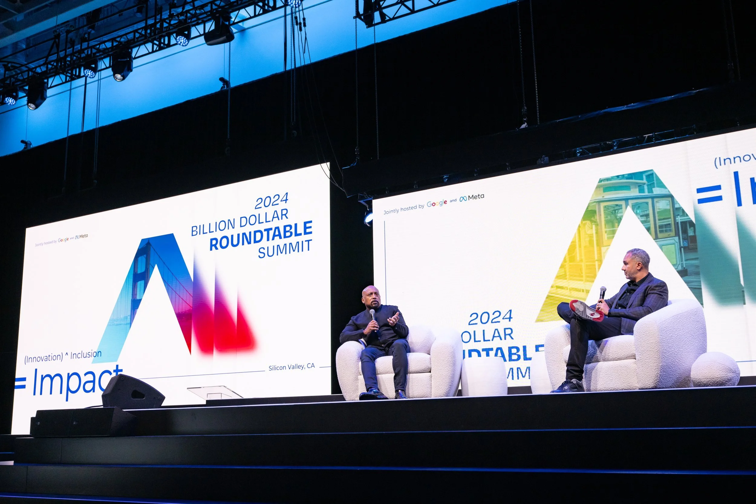 Two men seated on a stage with large screens behind them at a conference called the 2024 Billion Dollar Roundtable Summit. The screens display the event name and logos of Google and Meta as hosts.