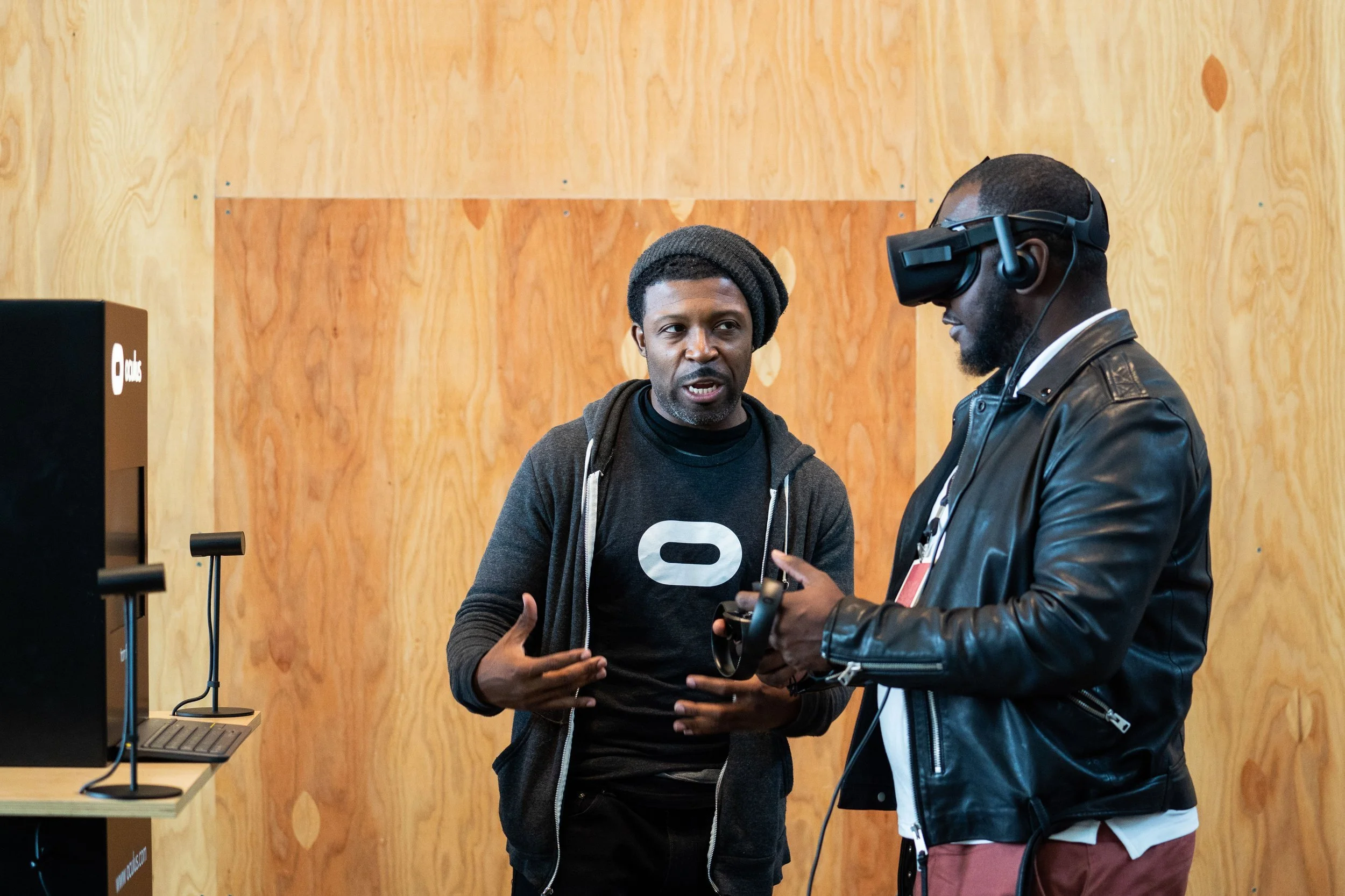 Two men engaging in a conversation at a tech event, with one wearing a virtual reality headset.