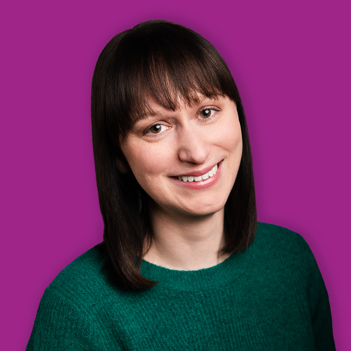 A smiling woman with shoulder-length dark hair and bangs, wearing a green sweater, against a purple background.