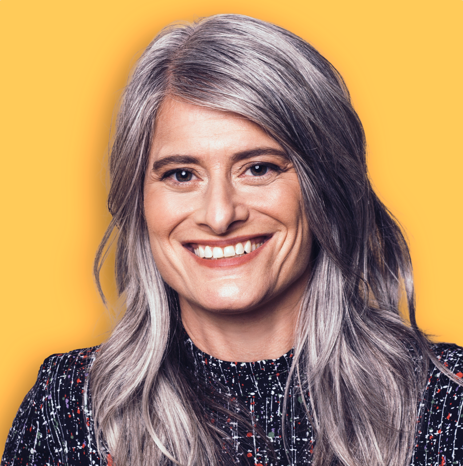 A smiling woman with long, gray hair against a yellow background.