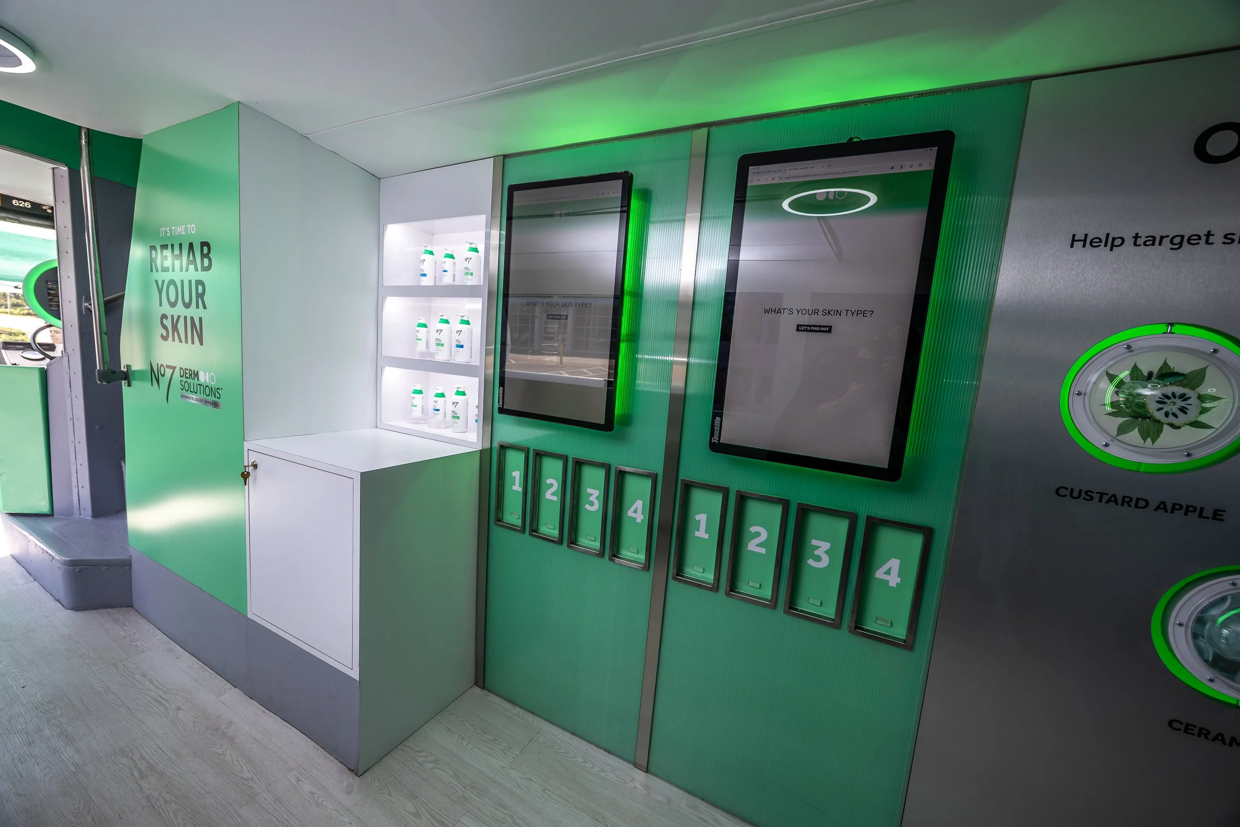 Inside a retail store, a digital screen asks 'What's your skin type?' with a green theme, shelves of skincare bottles, and numbered lockers beneath the screens.