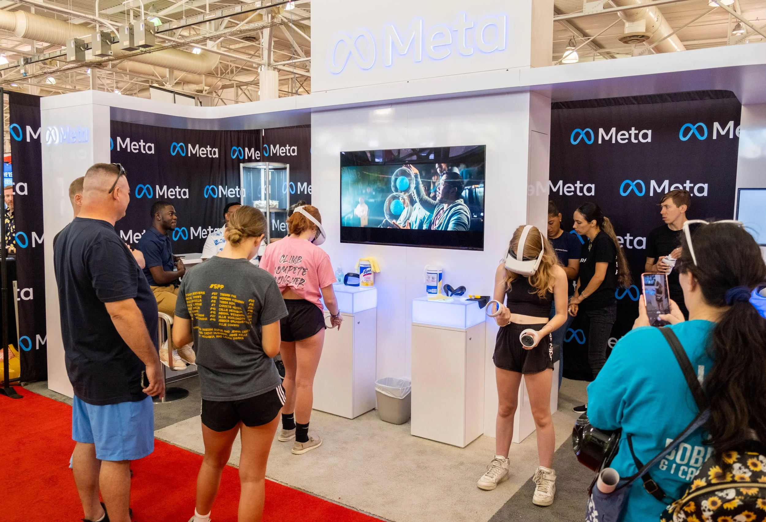 People attending a Meta booth at a convention or expo, with a large screen displaying a science or technology related image, and the booth decorated with Meta branding.