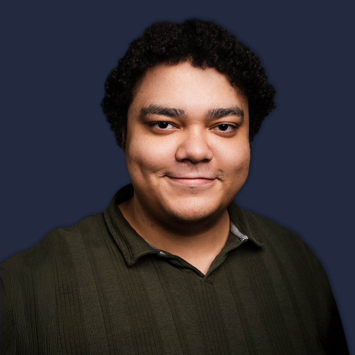 Headshot of a young man with curly dark hair, smiling, wearing a dark green shirt, against a dark blue background.