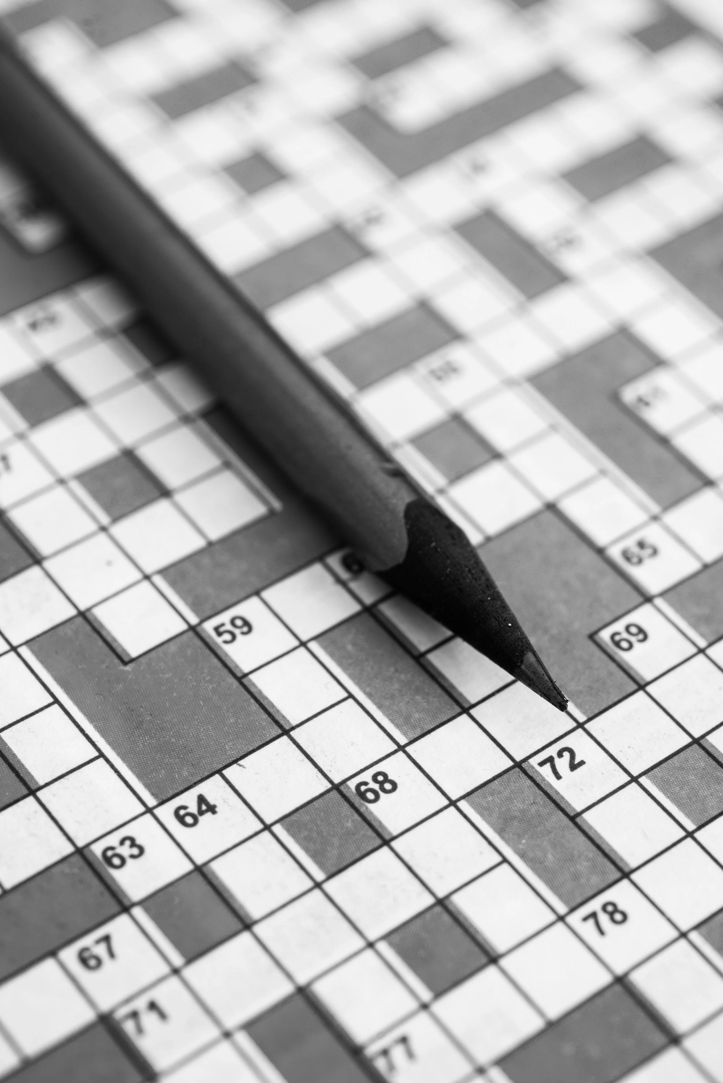 Fotografía en blanco y negro de una herramienta para resolver crucigramas, una pluma y una cuadrícula de crucigrama con letras y números.