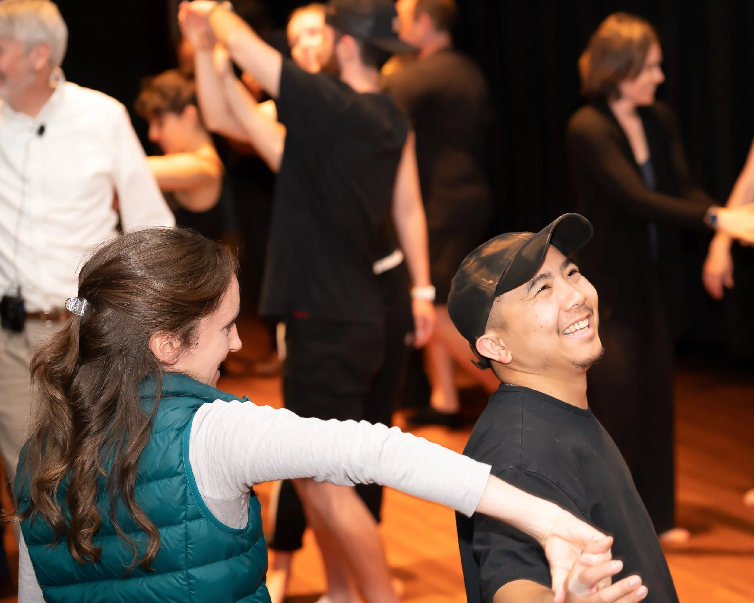 People dancing in a conga line, holding hands, in a lively indoor setting.