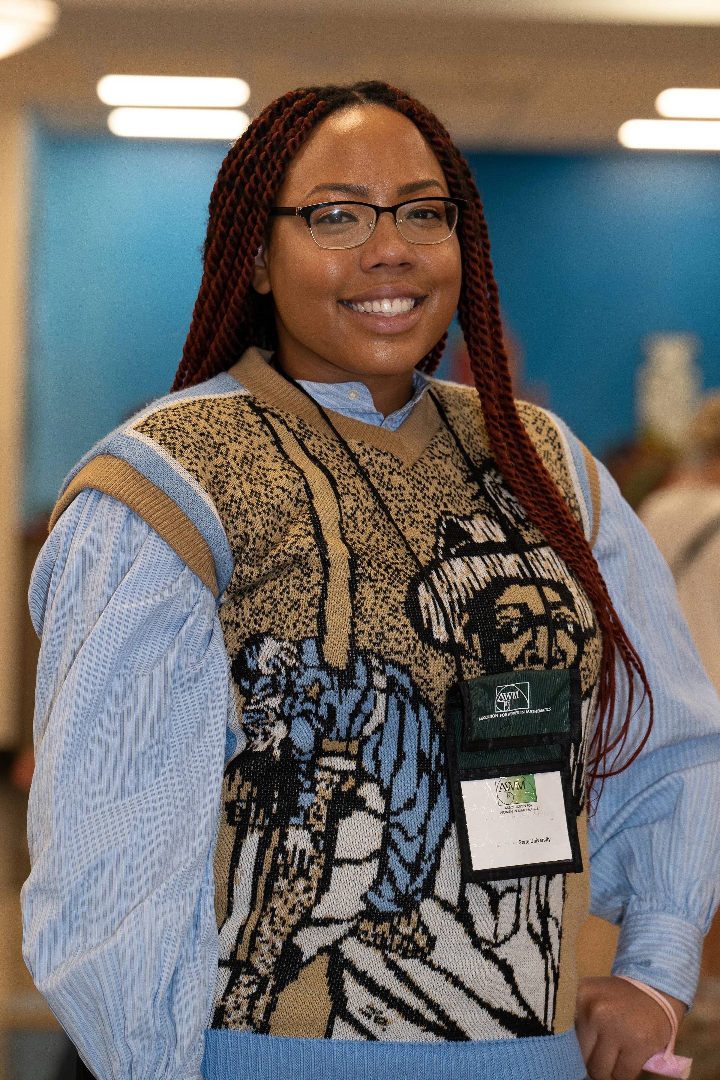 Woman with red braided hair wearing glasses and a sweater with a tiger print, standing indoors with blue walls in the background.