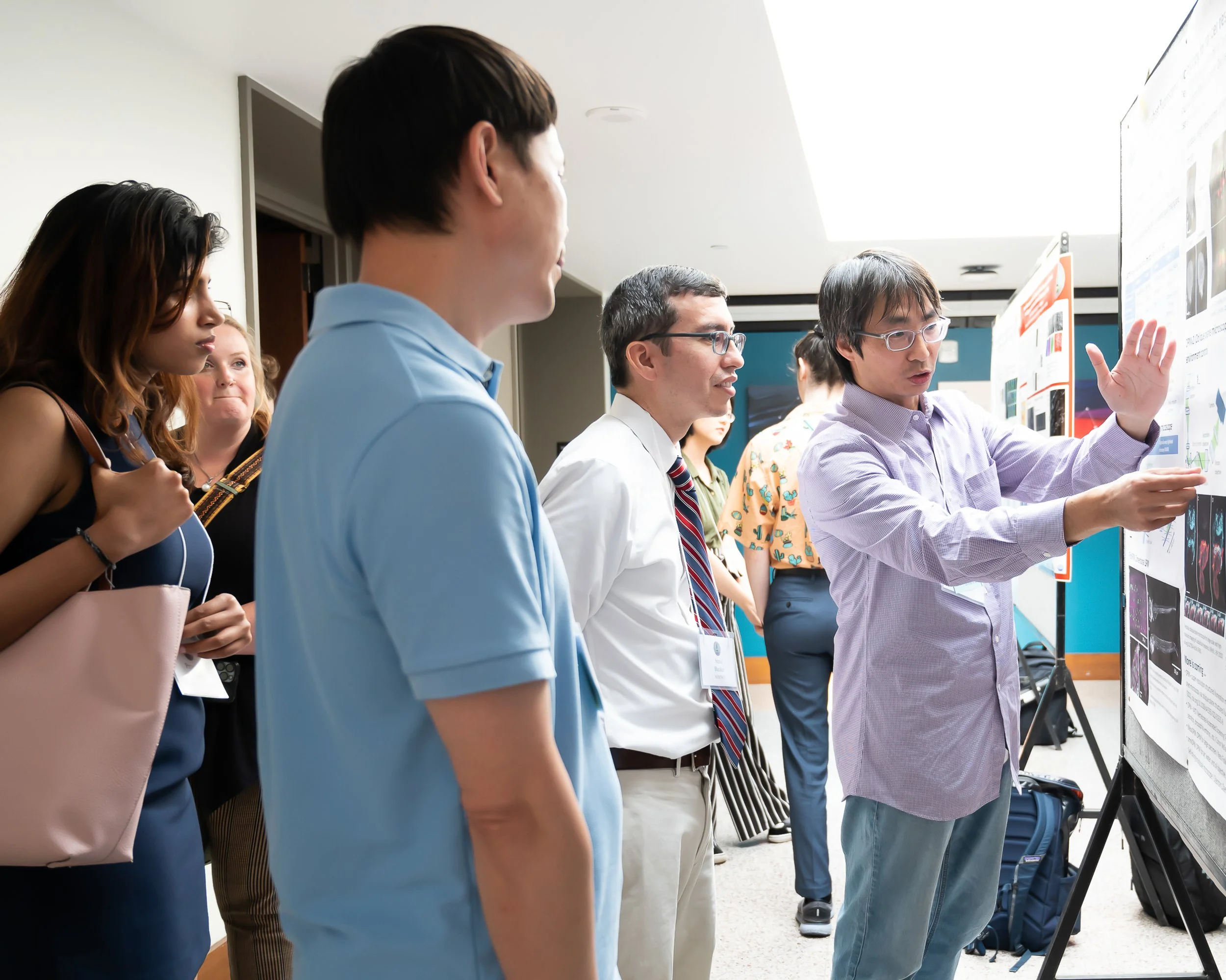 Group of people at a scientific conference looking at research posters, one person explaining findings to others.