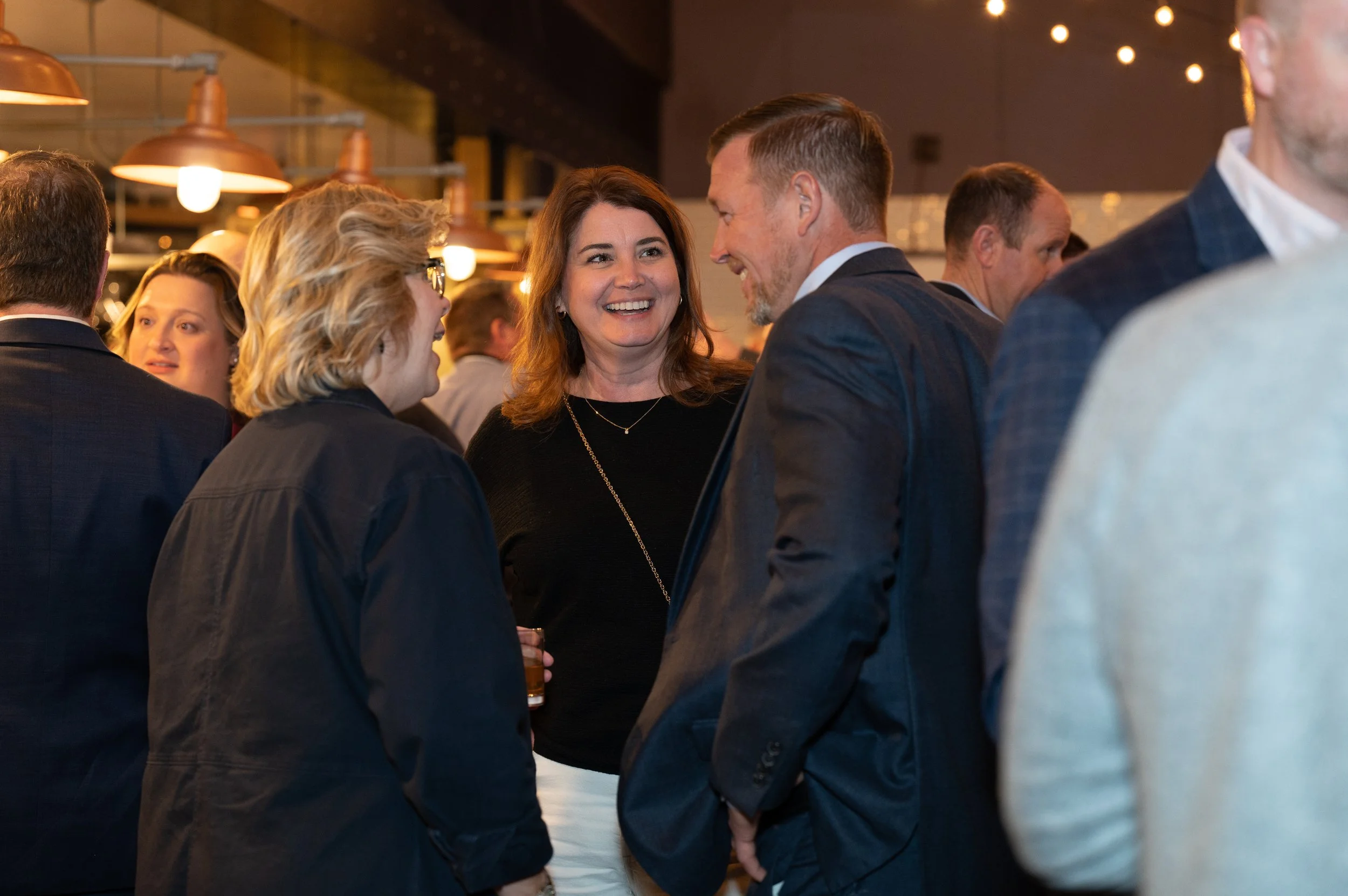 People in business attire at a social event, engaged in conversation and smiling.