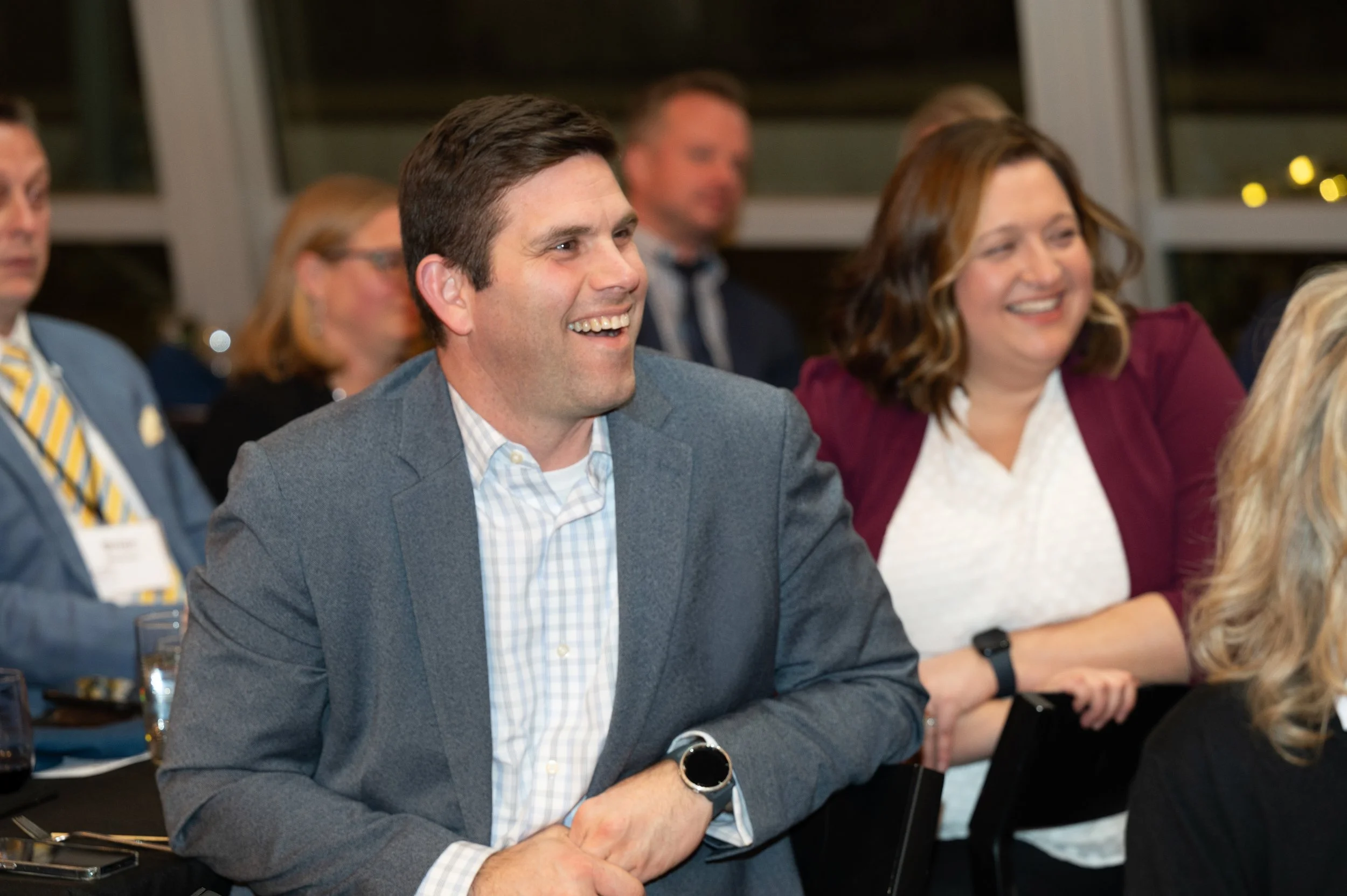 A group of people in business attire attending a conference or meeting, with a man and a woman smiling and engaging with the event.