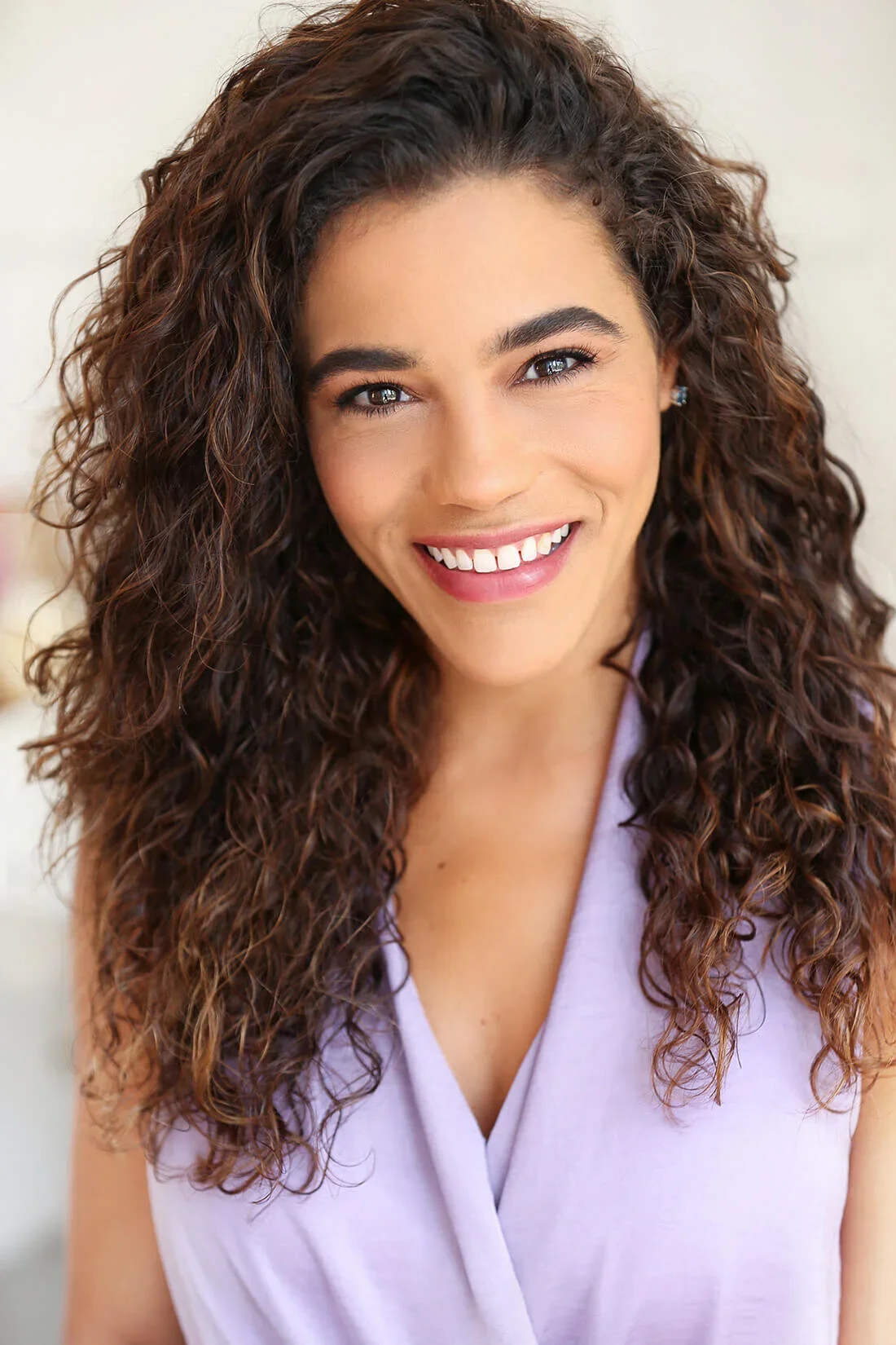 A smiling woman with curly dark brown hair wearing a light purple top.