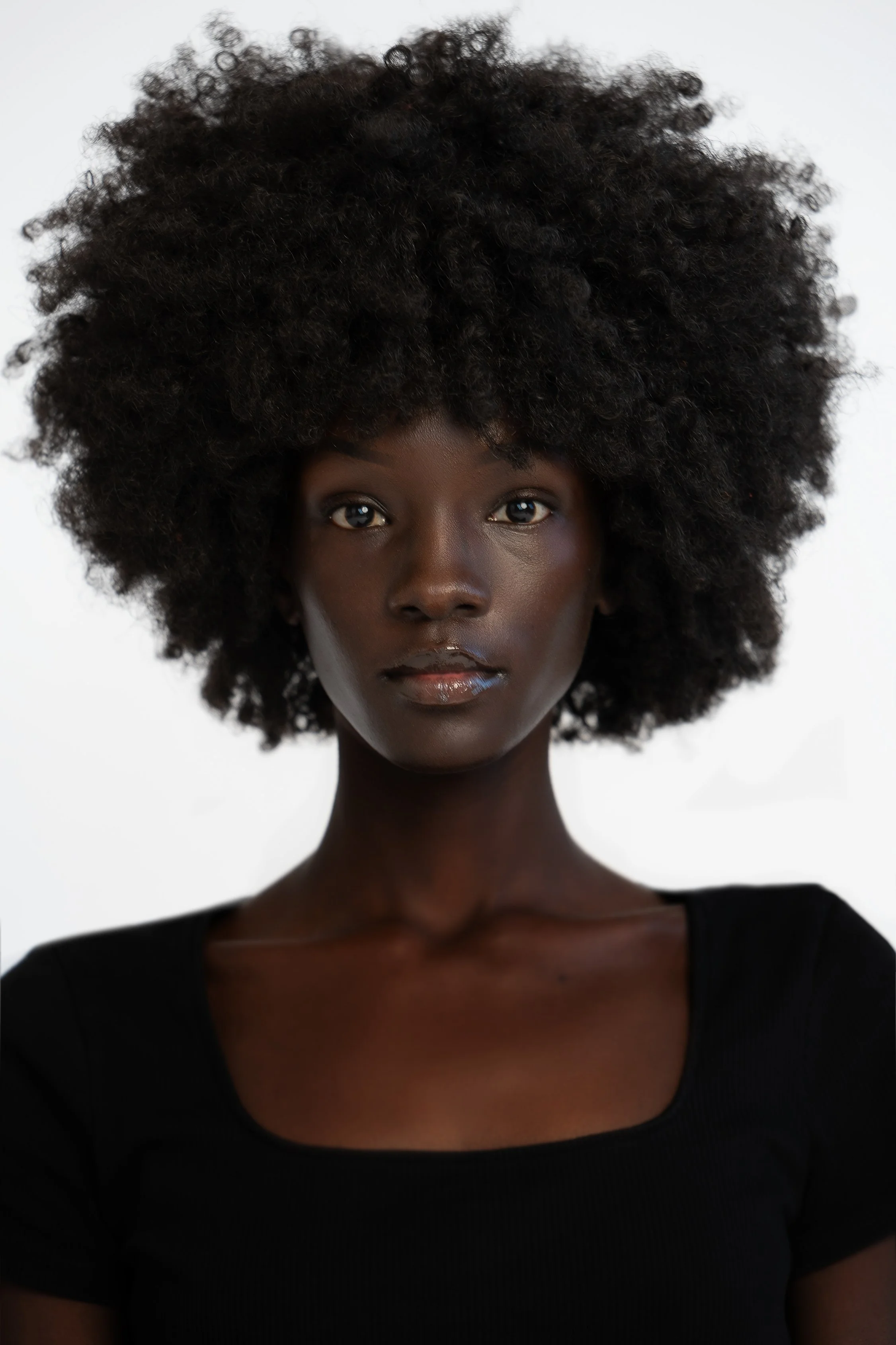 Portrait of a woman with large, natural afro hair, wearing a black top, against a plain white background.