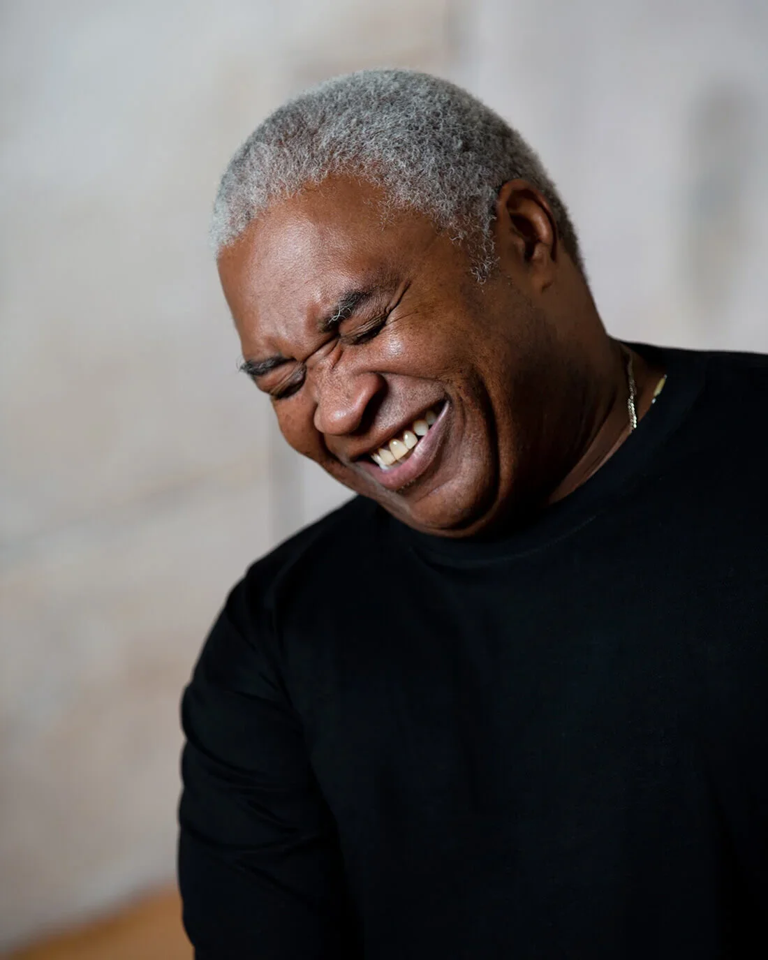An elderly man with gray hair smiling and laughing, wearing a black shirt.