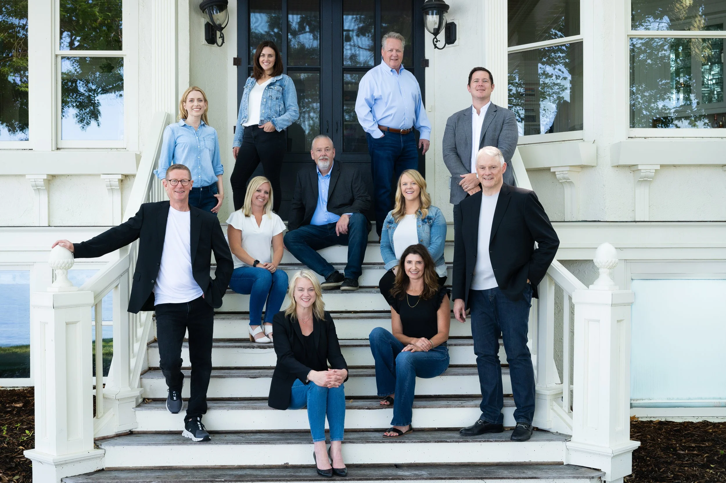 Group of ten people, men and women, gathered on front stairs of a house, smiling for a photo.