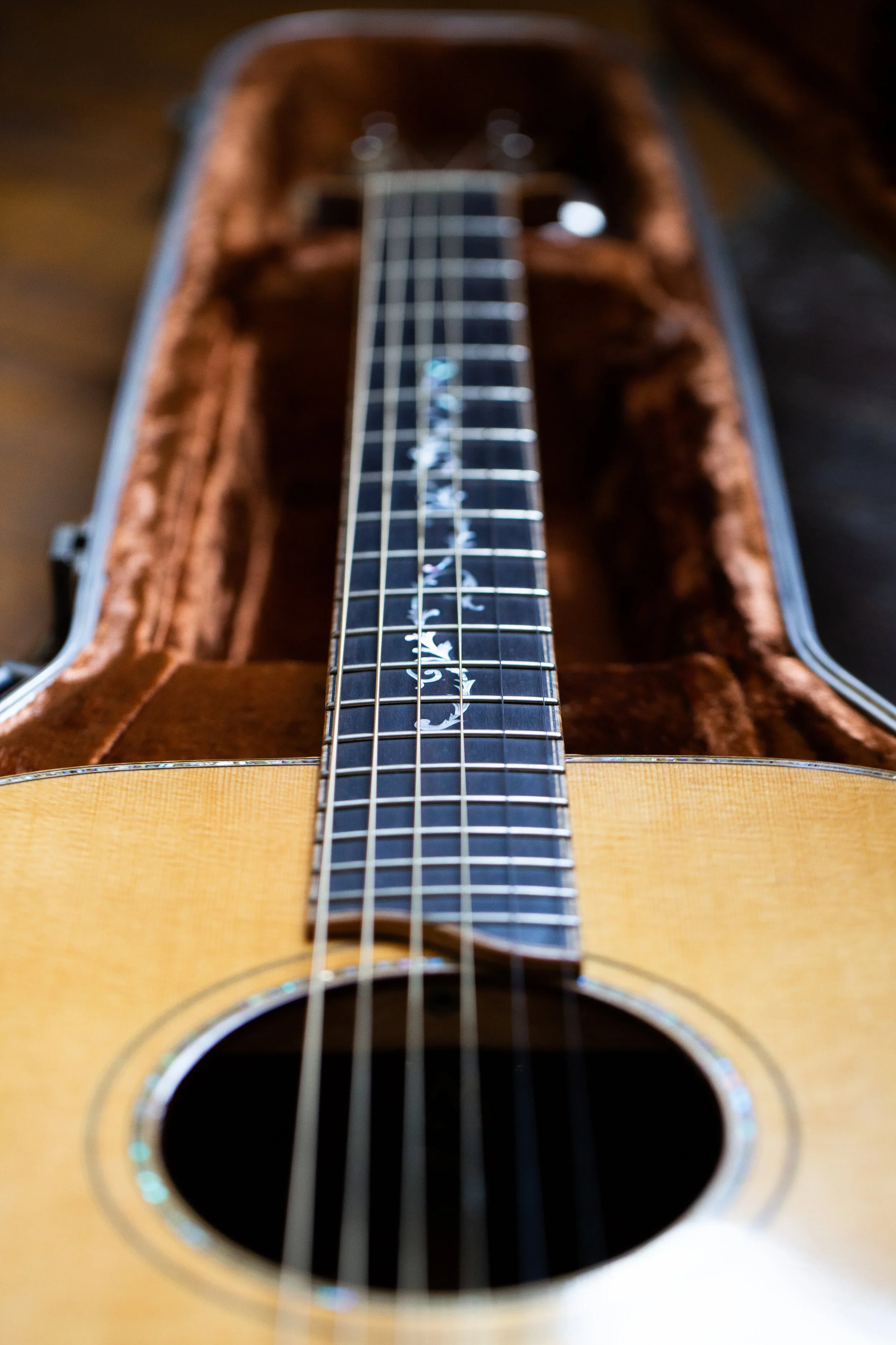 Close-up of an acoustic guitar with a decorative fretboard inlay, inside a brown plush-lined case.