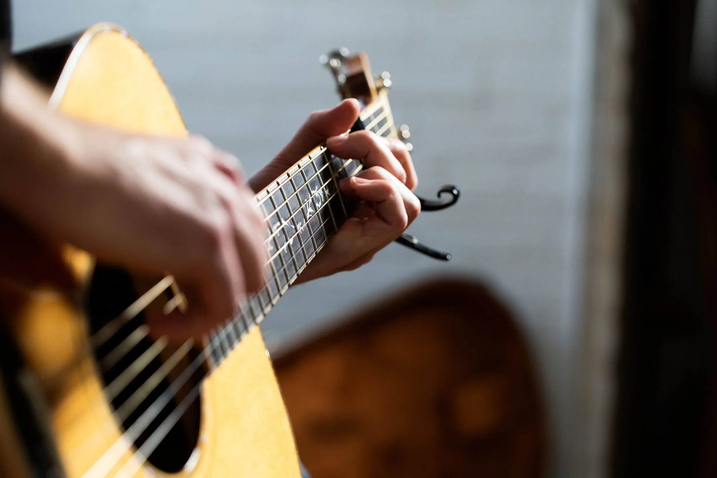 Close-up of a person’s hand strumming an acoustic guitar with a blurred background.