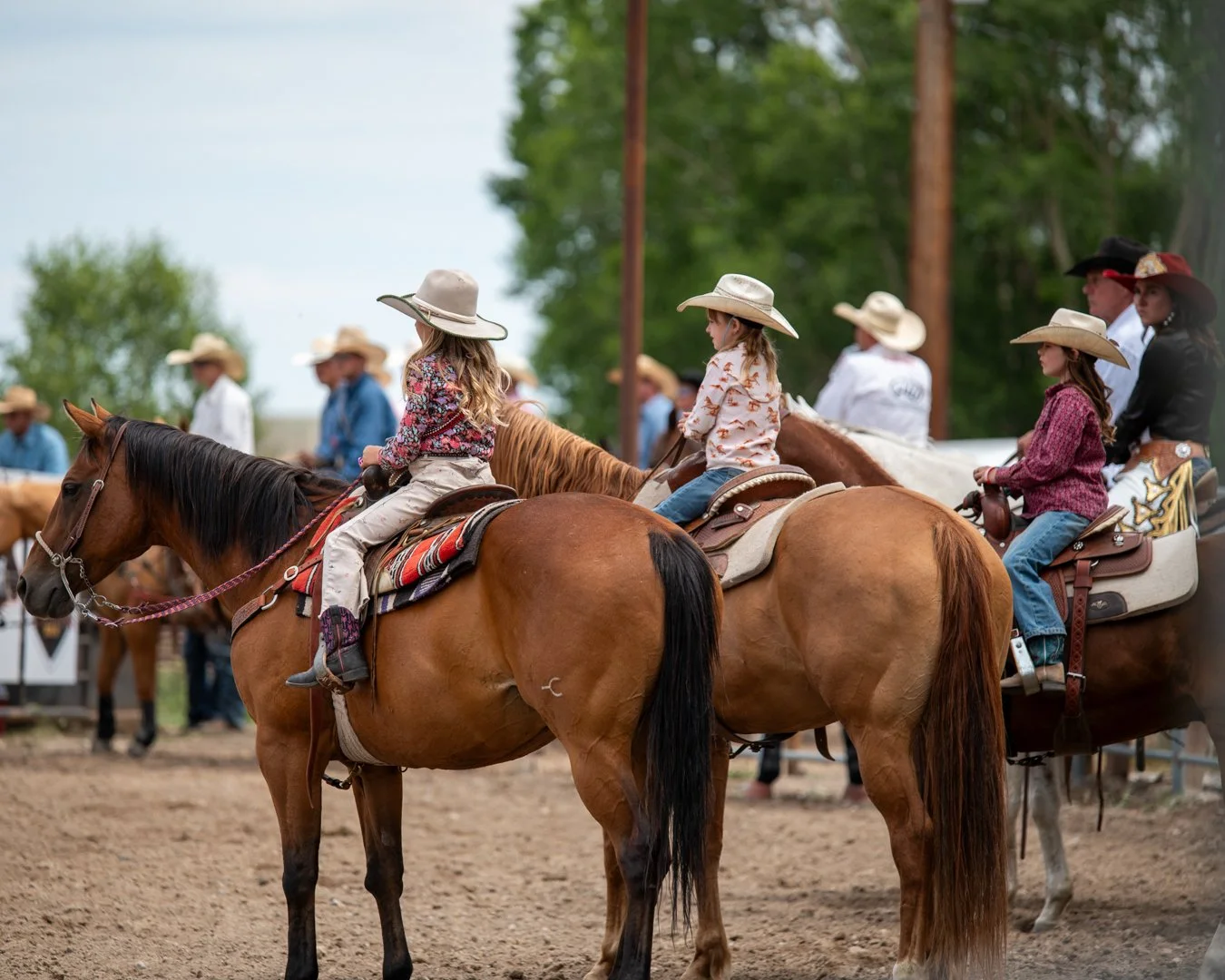 Group of children and adults riding horses at a rodeo or western event, wearing cowboy hats and western attire.