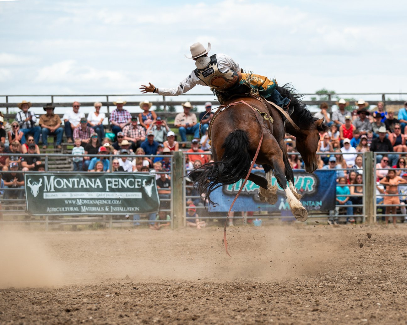 A cowboy riding a bucking horse during a rodeo event in front of a crowd of spectators.