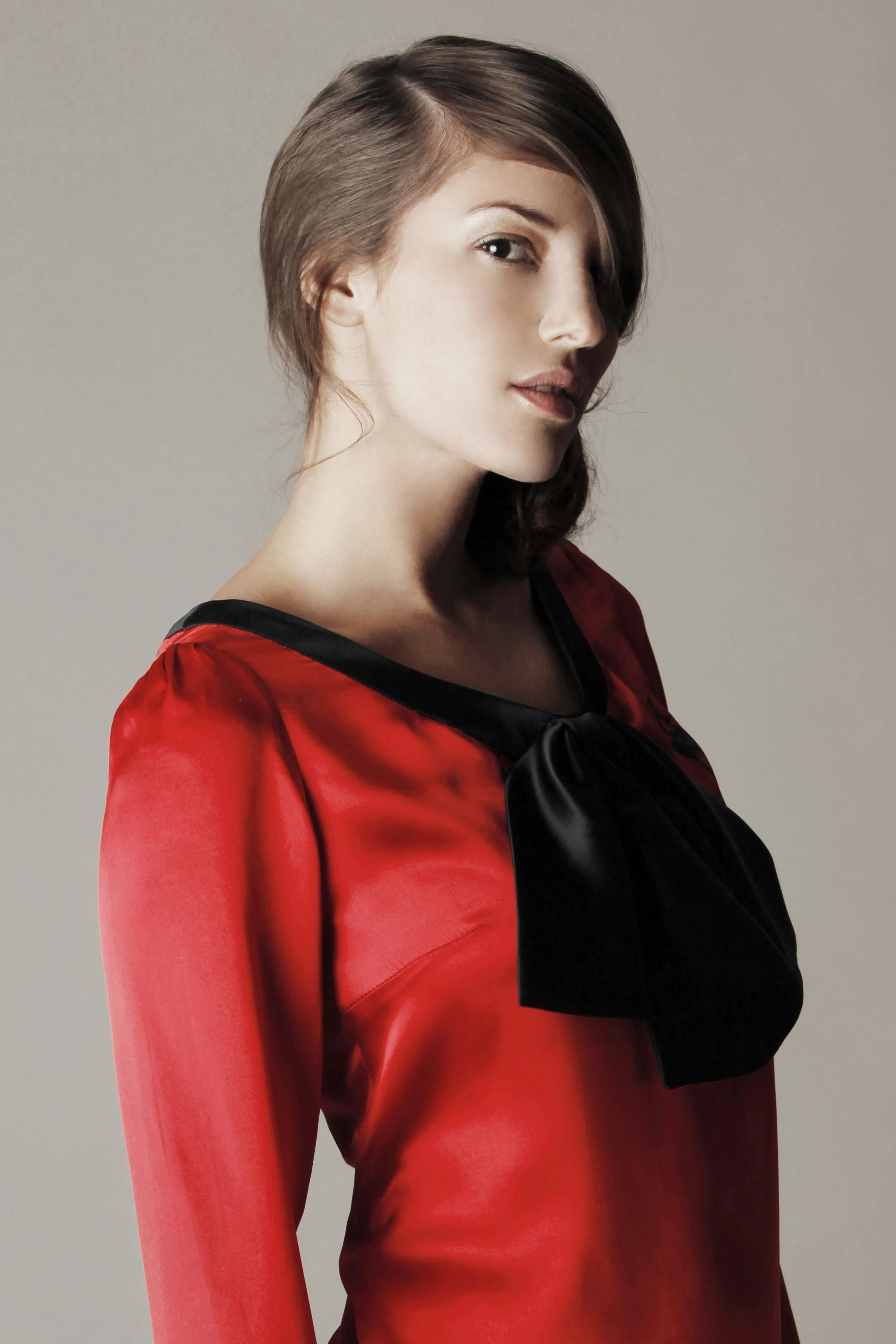 Portrait of a woman with short, dark brown hair styled to one side, wearing a red and black satin dress, against a plain background.