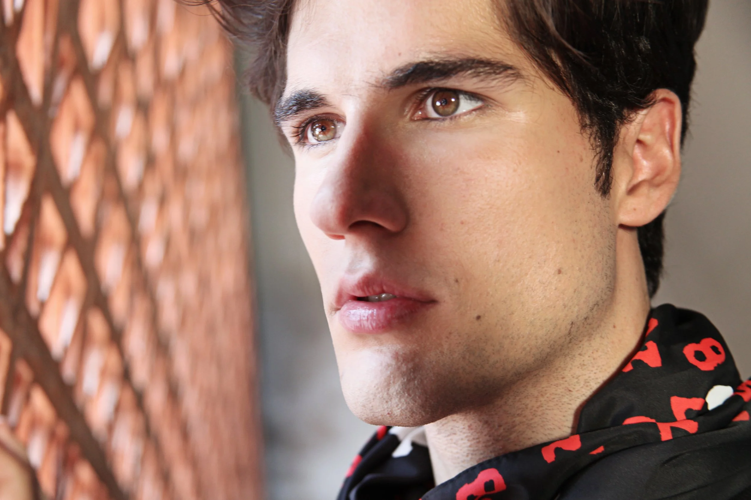 Close-up of a person with dark hair, light skin, and brown eyes, looking to the right, against a blurred background with wooden texture.