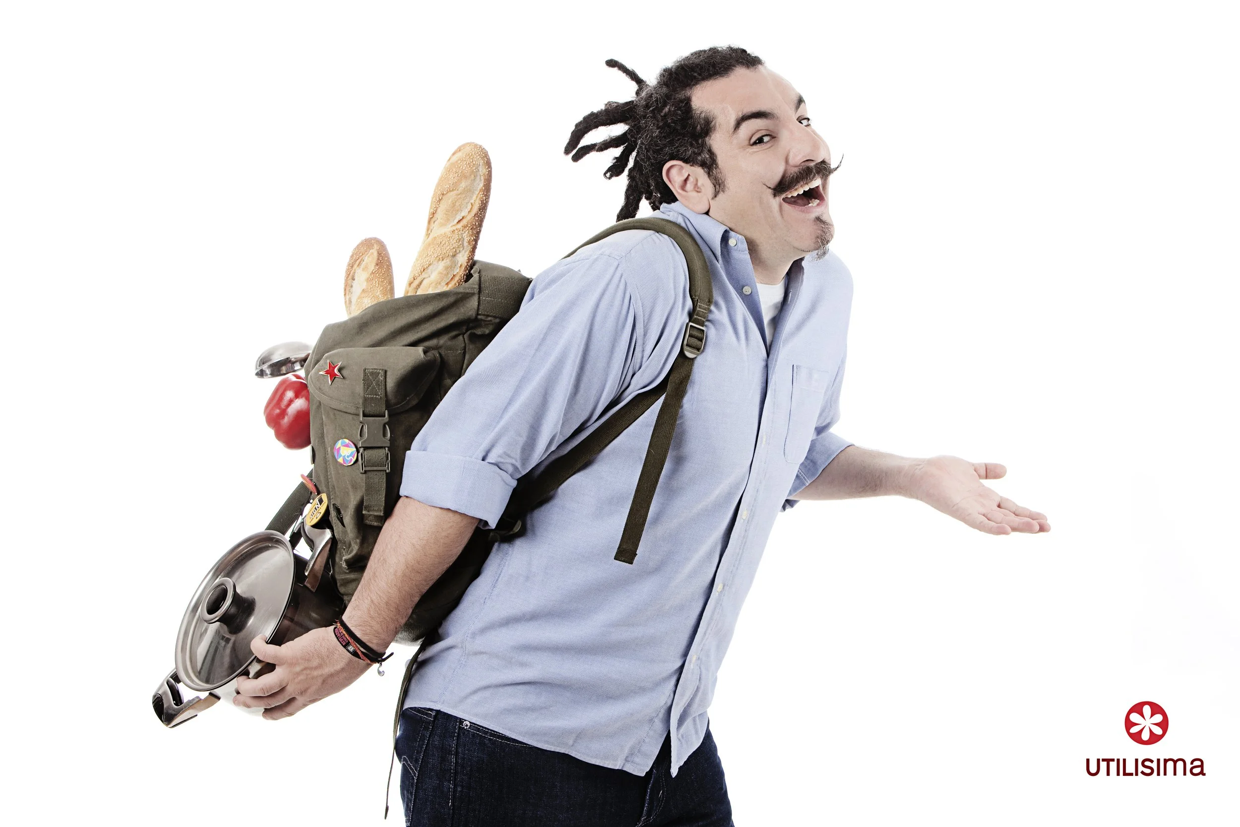 A man with dreadlocks and a mustache wearing a light blue shirt and jeans, leaning forward with his mouth open, and a backpack with baguettes, a red pepper, and other items inside, against a white background.