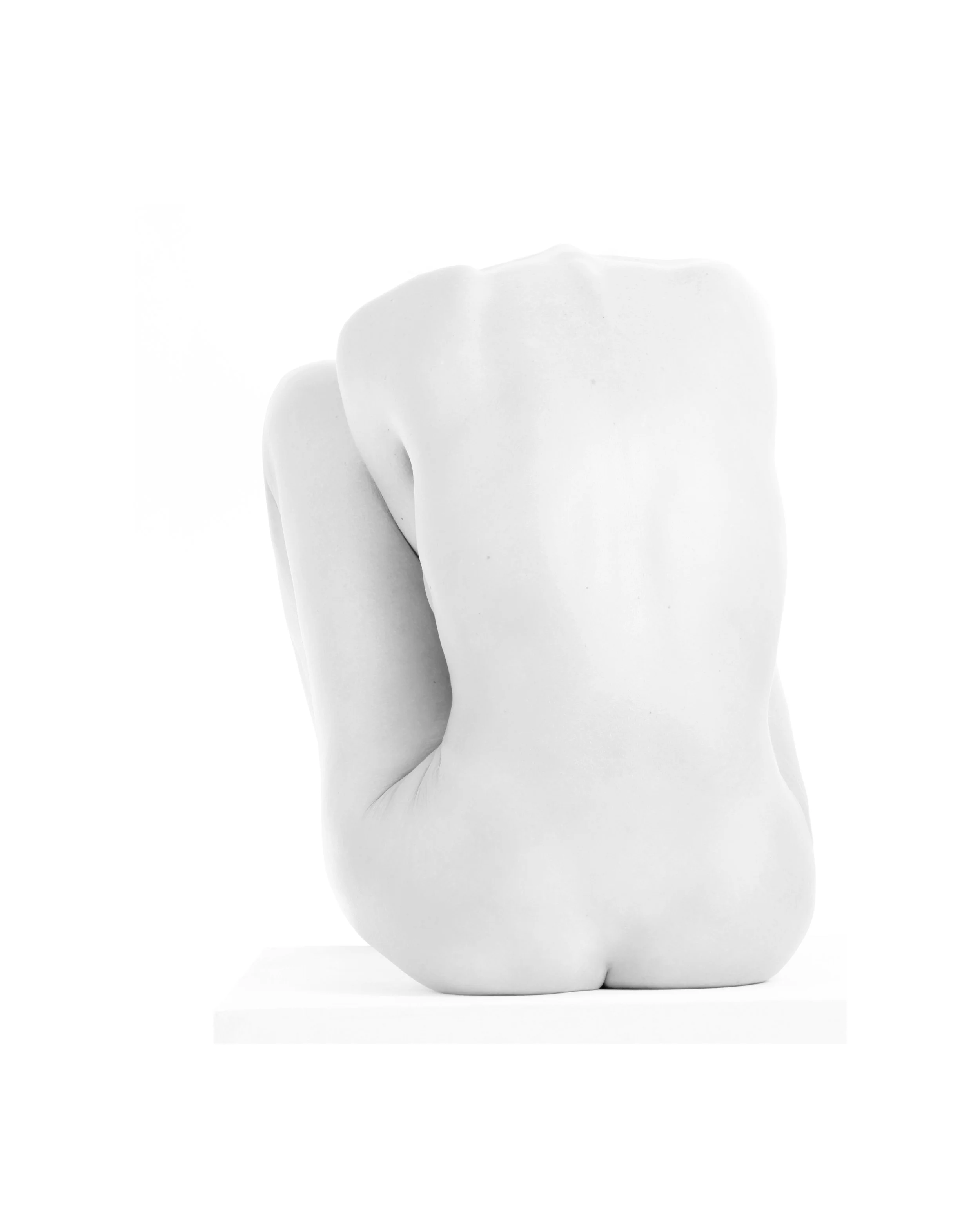 A white sculpture of a human hand with fingers curled into a fist, positioned against a white background.