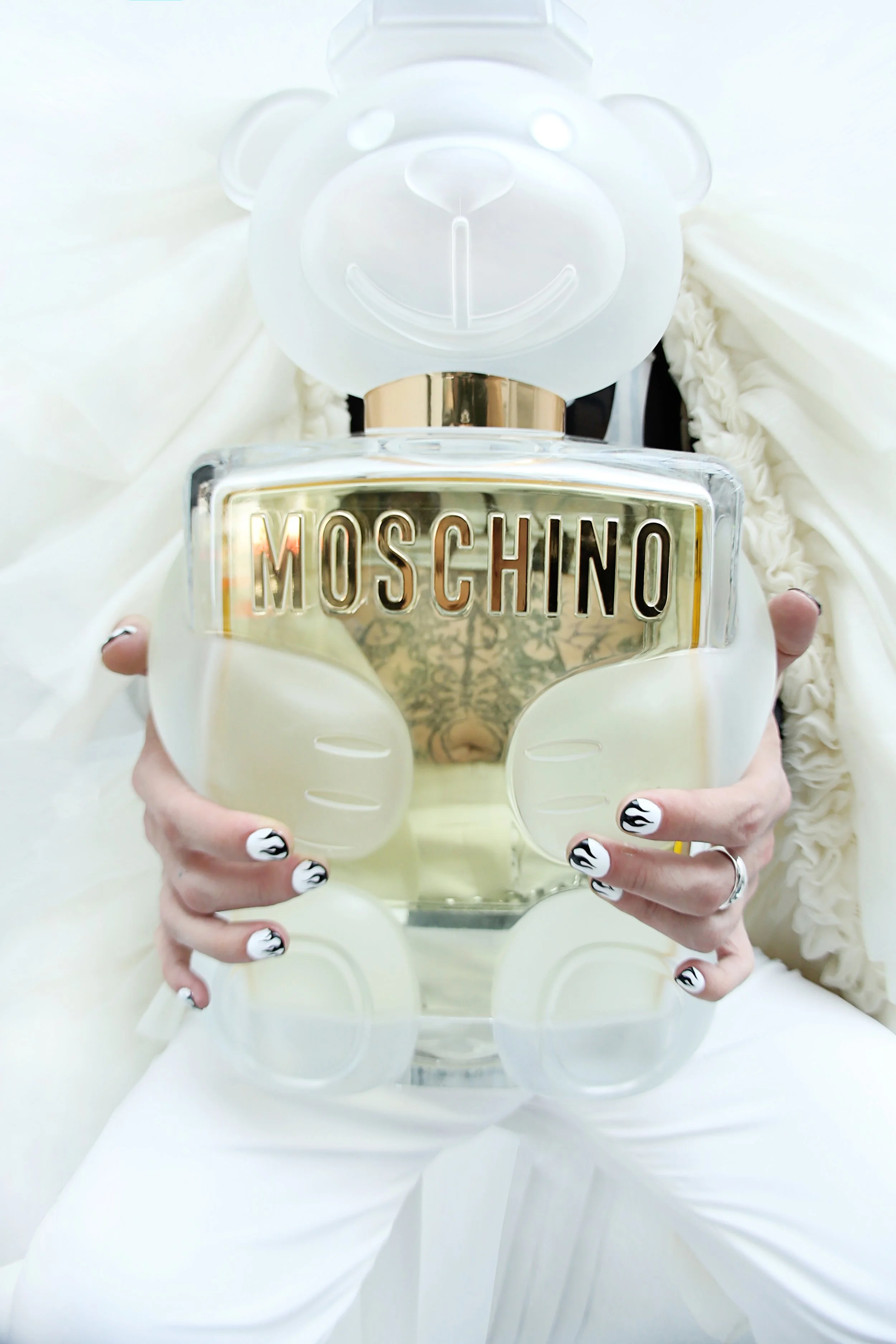 Person holding a Moschino perfume bottle designed as a teddy bear with a gold and clear label.