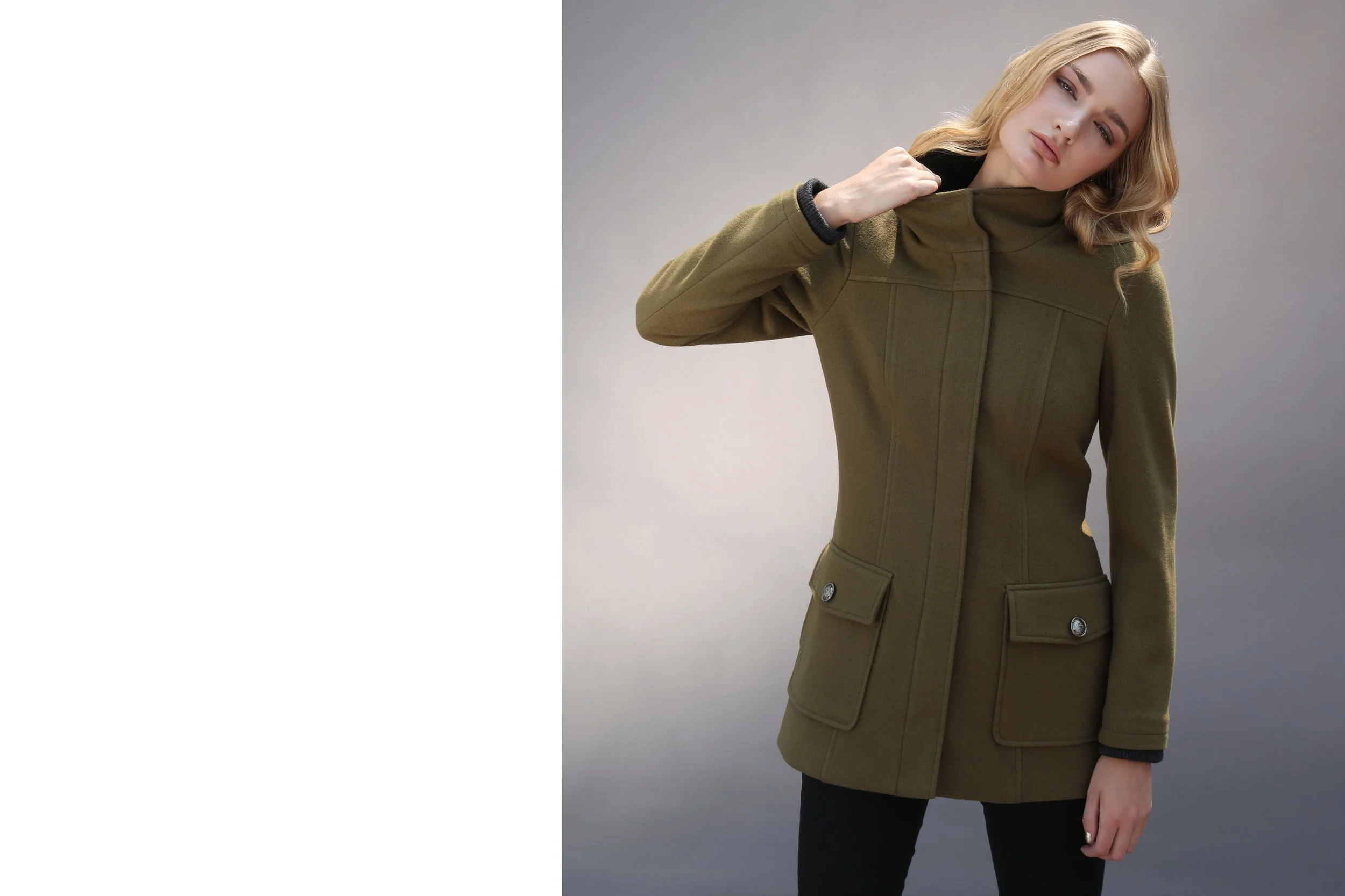 A woman with blonde hair wearing a green jacket and black pants against a gray background.