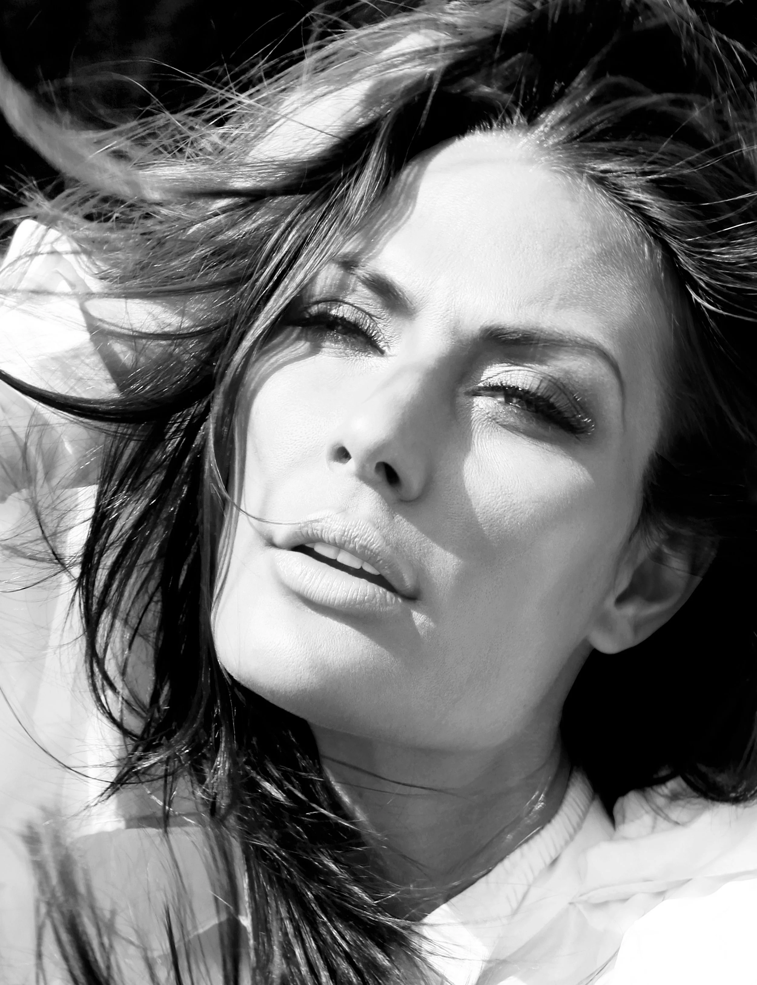 Black and white close-up of a woman's face with her eyes closed and her head tilted, with wind-blown hair.