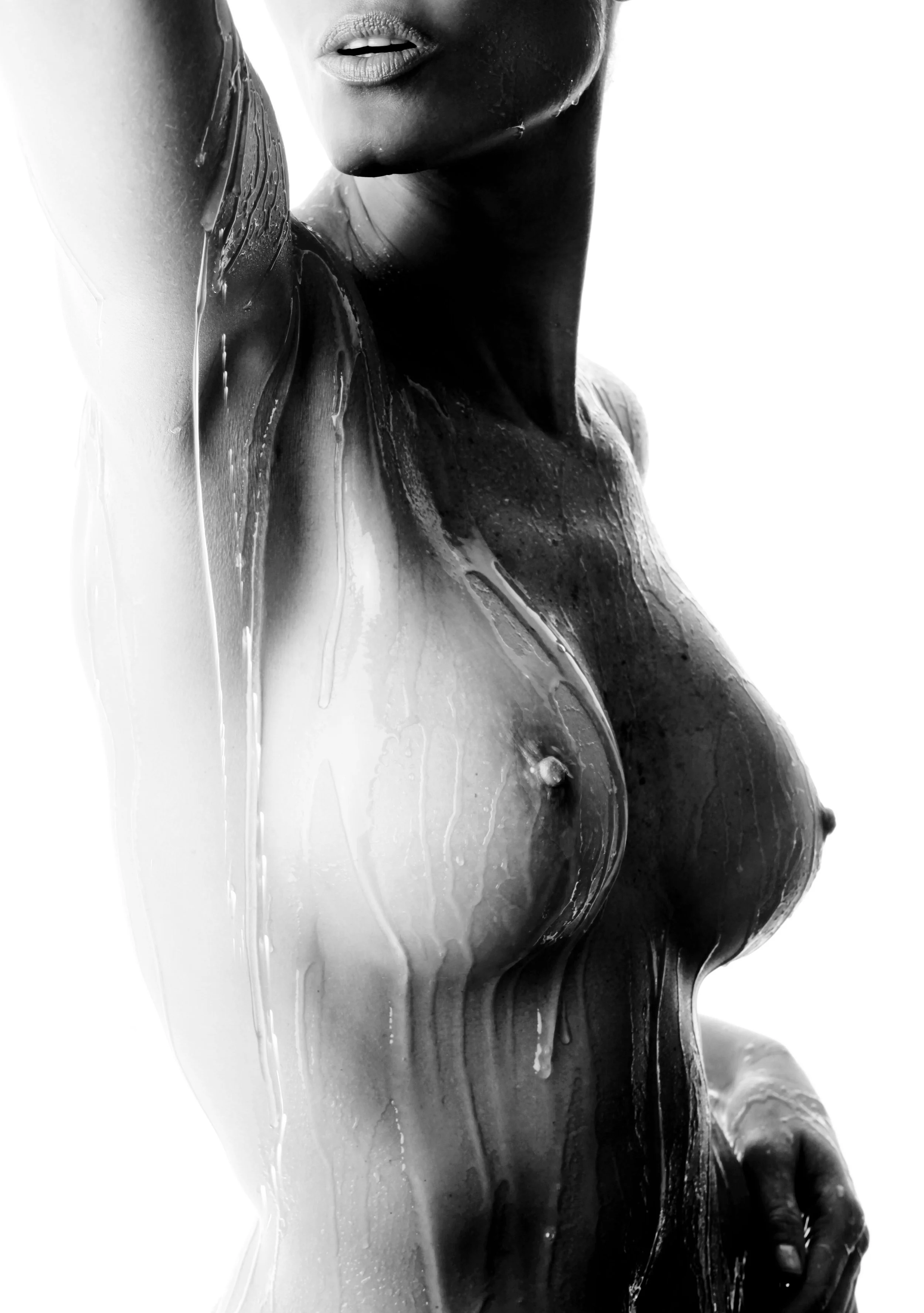 A close-up black and white photo of a woman with water pouring down her body, partially covering her face and chest, with her lips slightly parted.
