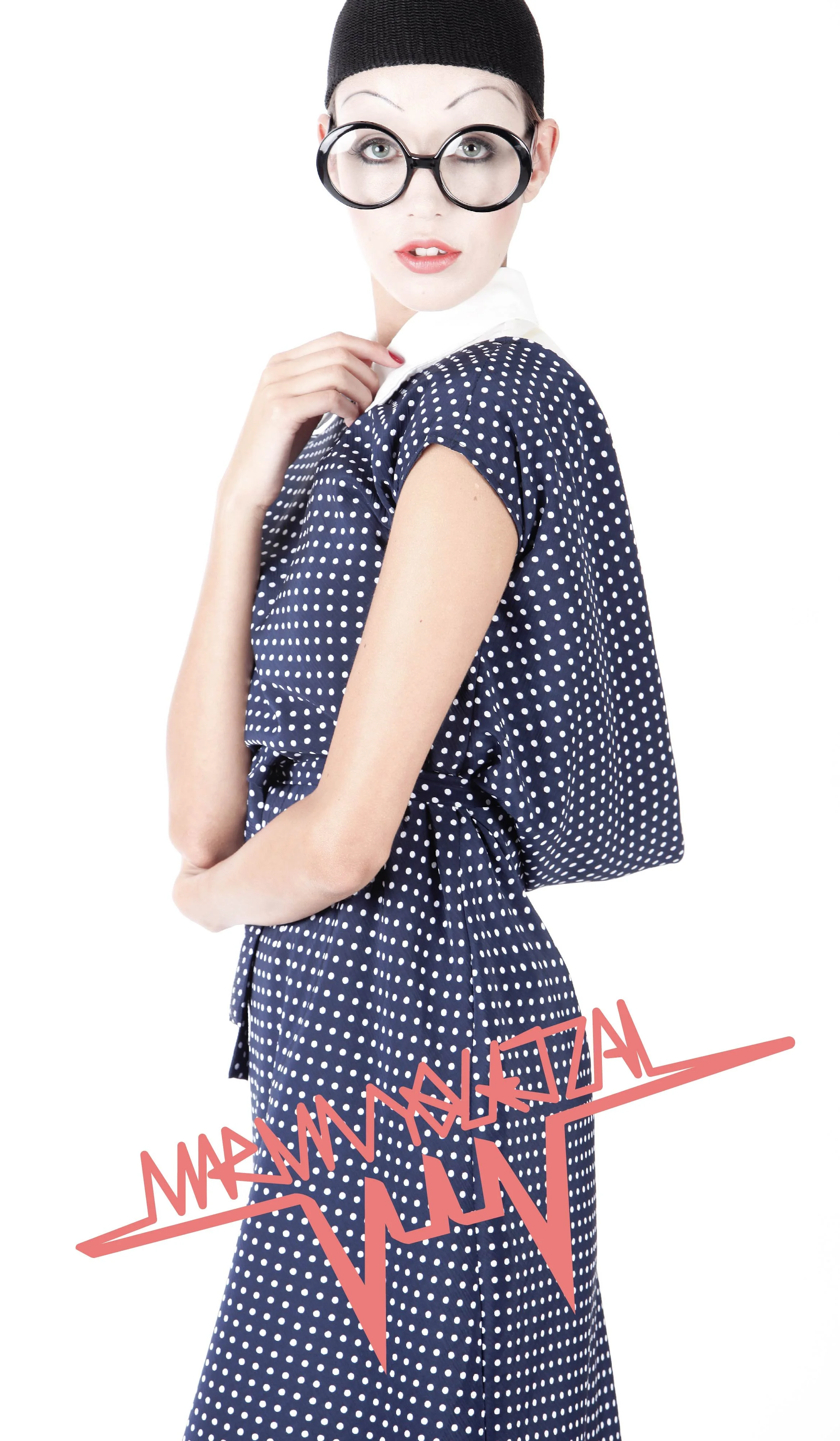 Fashionably dressed woman in a polka dot dress with glasses and a beanie, holding a bag over her shoulder, with a white background and digital text overlay.