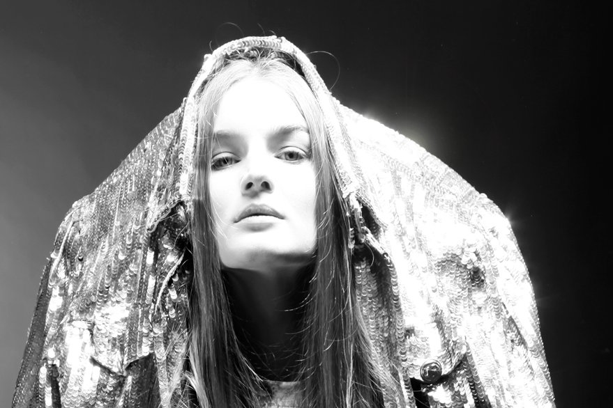 Black and white photo of a woman with long hair, wearing a sequin jacket with a hood over her head.