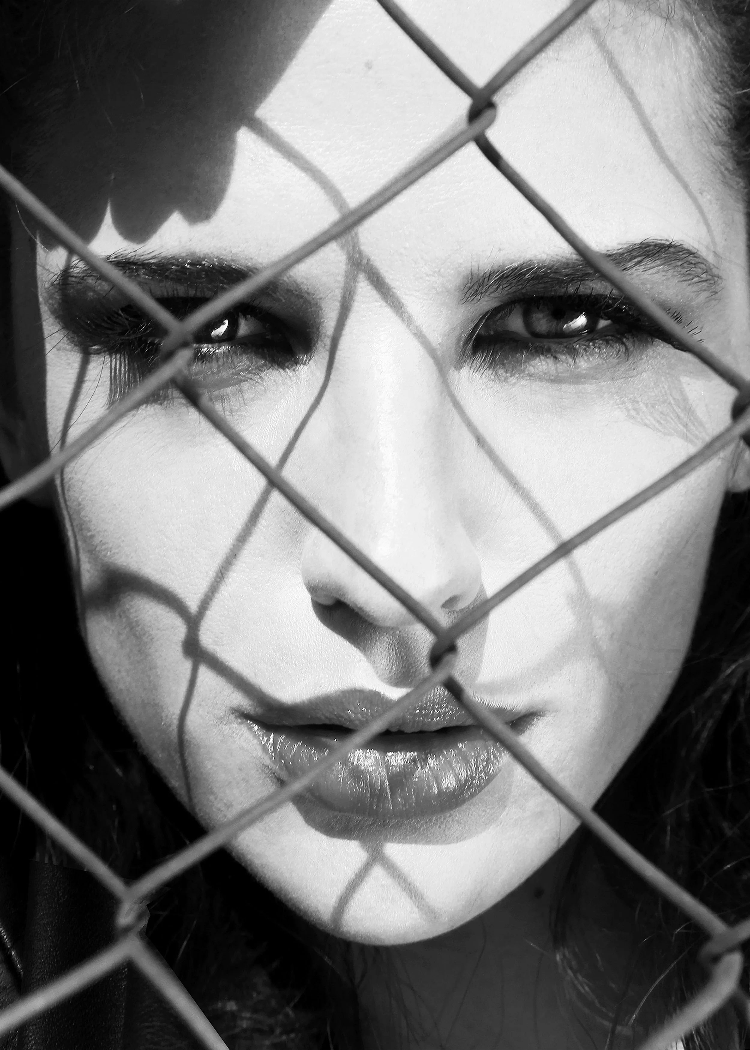 Close-up of a person's face behind a wire fence, showing eyes, nose, and lips in black and white.