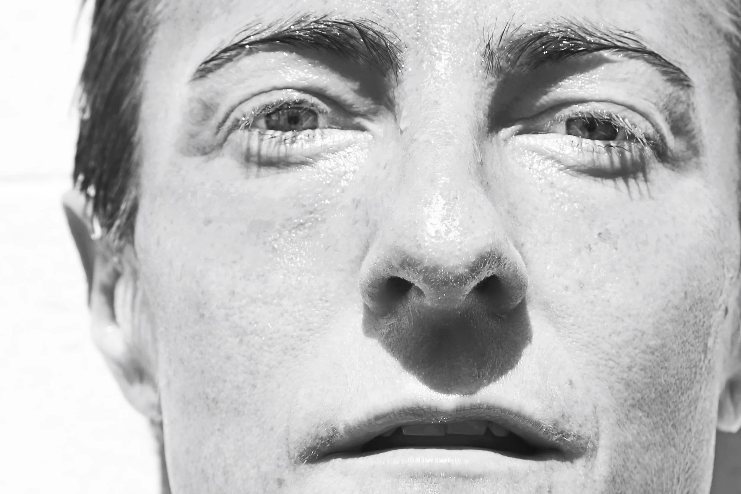 Close-up black and white photo of a person's face, with one eye open and the other eye winking, wet skin, and slightly parted lips.