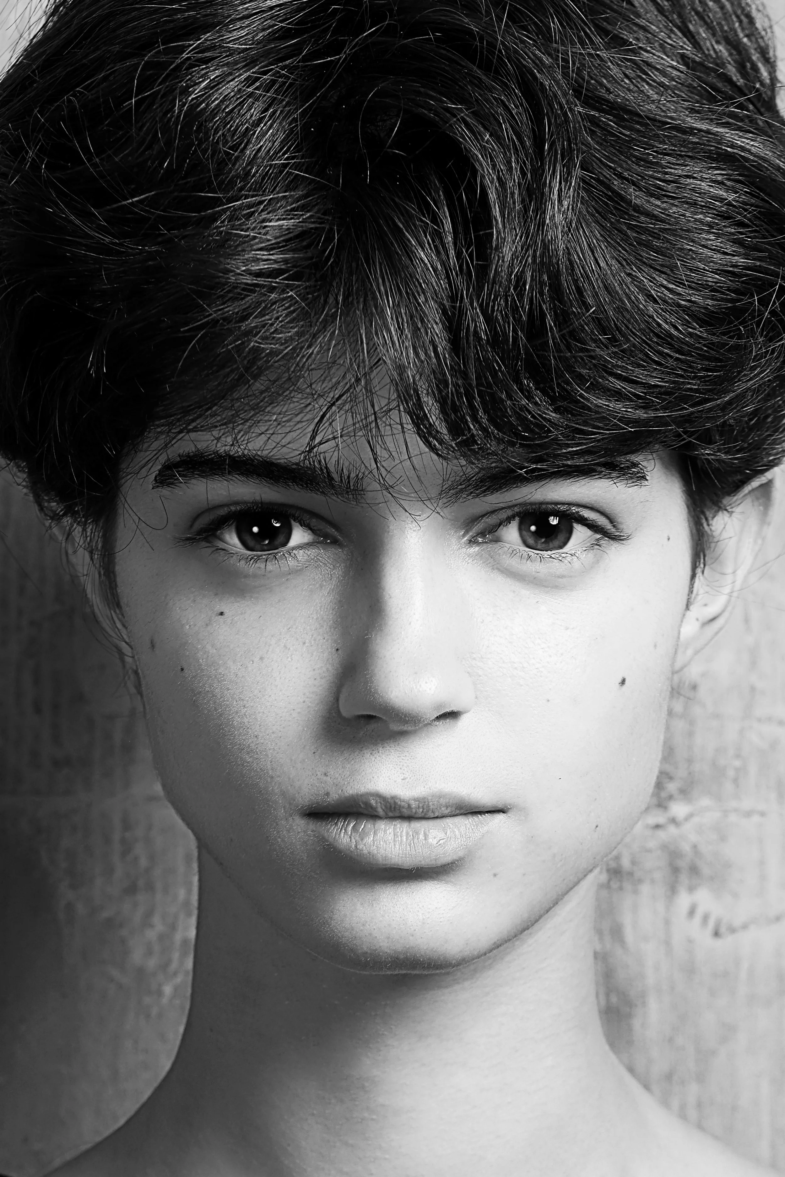 Close-up black and white portrait of a person with textured short hair, expressive eyes, clear skin, and slightly parted lips.