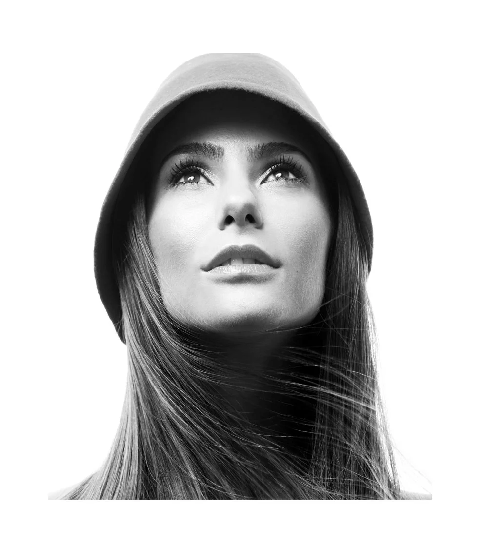 Black and white portrait of a woman wearing a hoodie, looking upwards with long hair flowing, high contrast lighting.