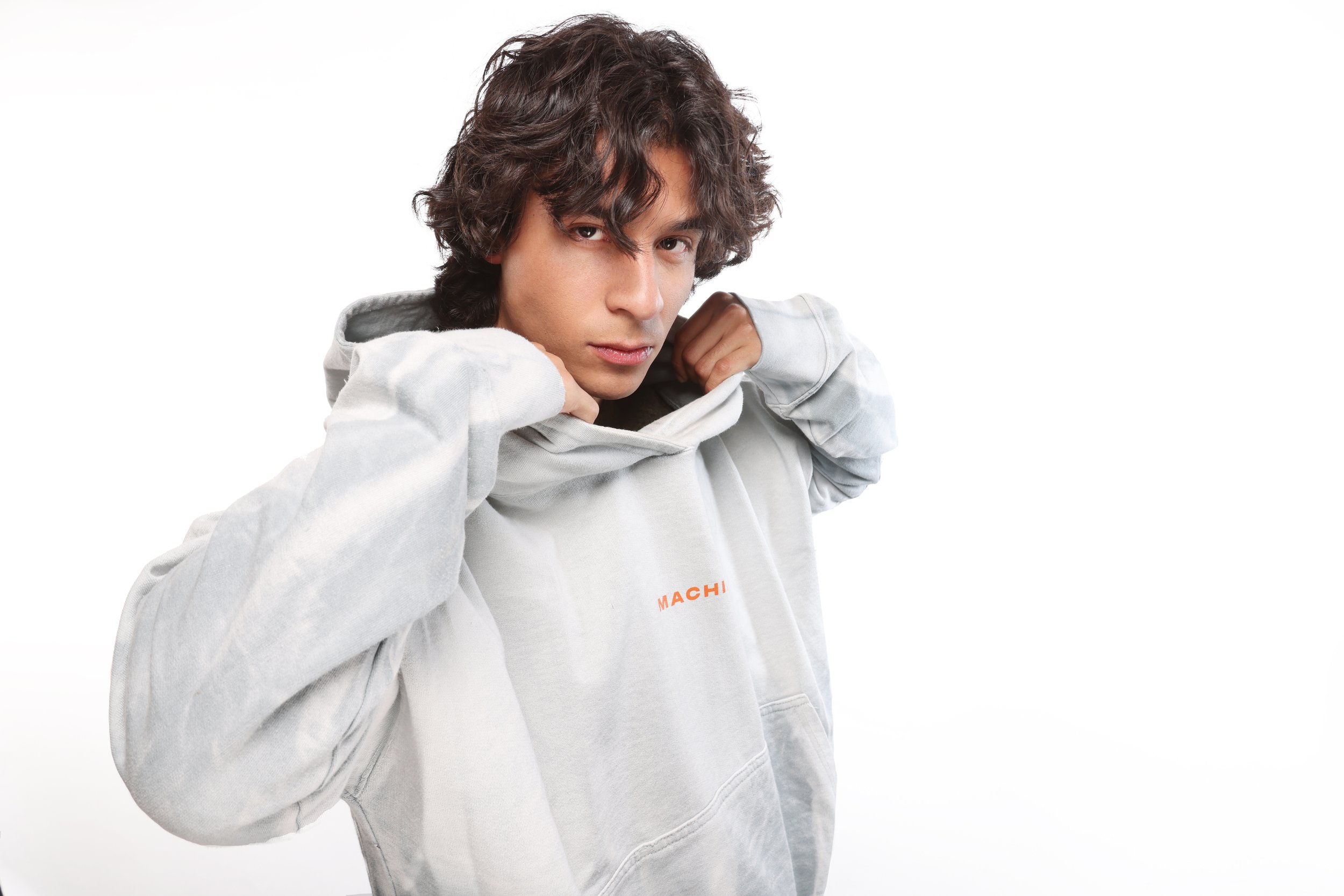 Young man with curly dark hair wearing a light gray hoodie, looking at camera, against a white background.