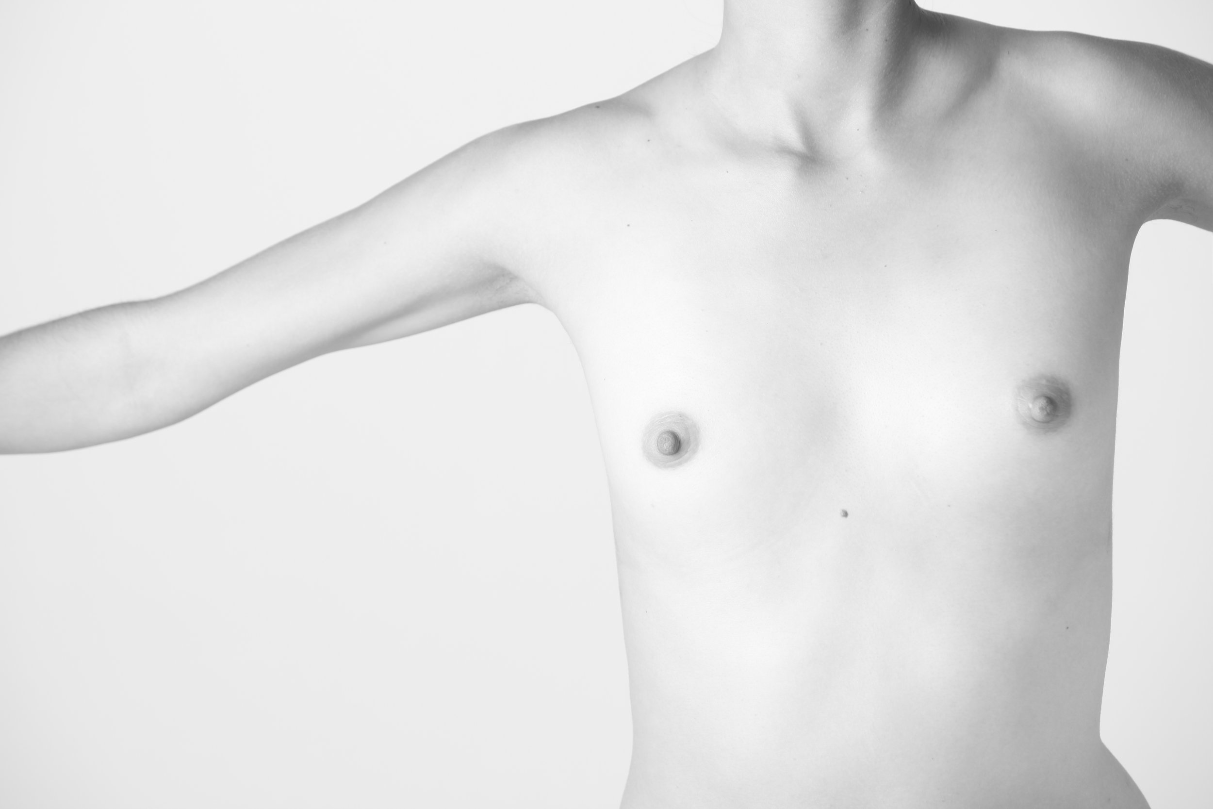 Black and white photograph of a partially nude woman with her arm extended, showing her torso, breasts, and the side of her face and neck.